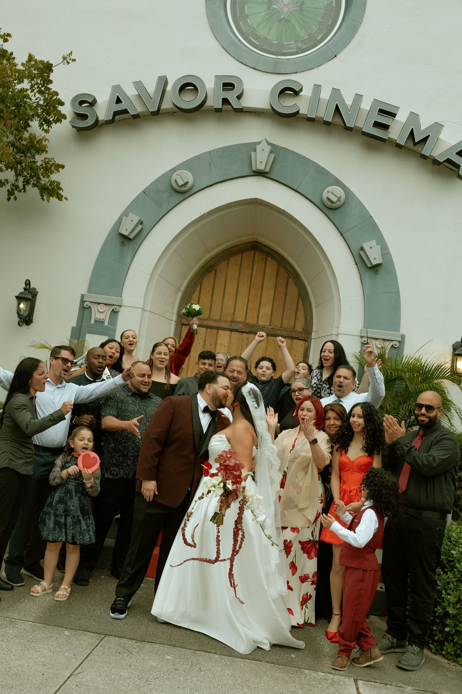 A group of wedding guests gather outside the entrance of Savor Cinema for a celebratory photo.
