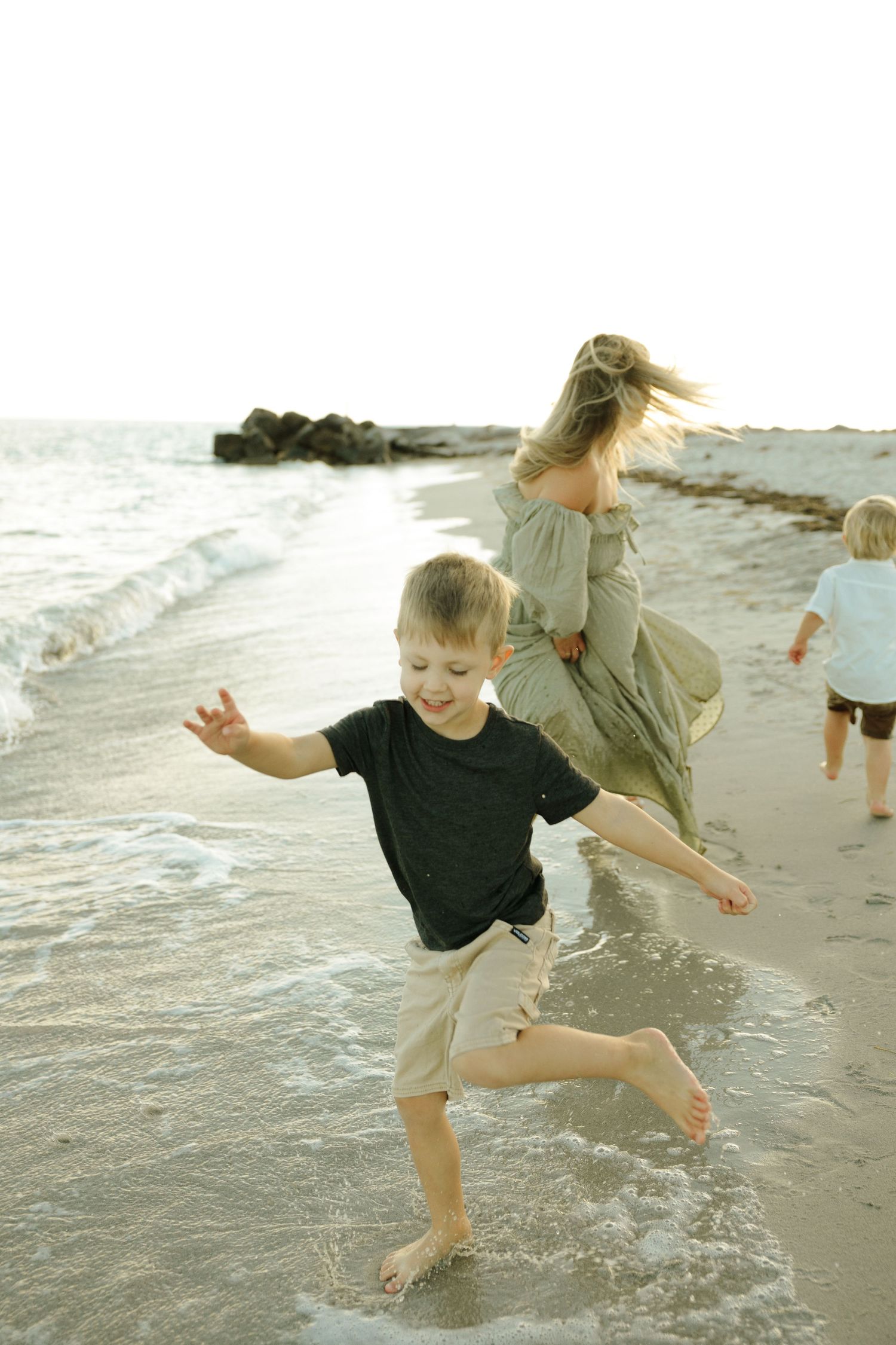 Family playing and splashing together in the shallow ocean waves at sunset on a peaceful beach.