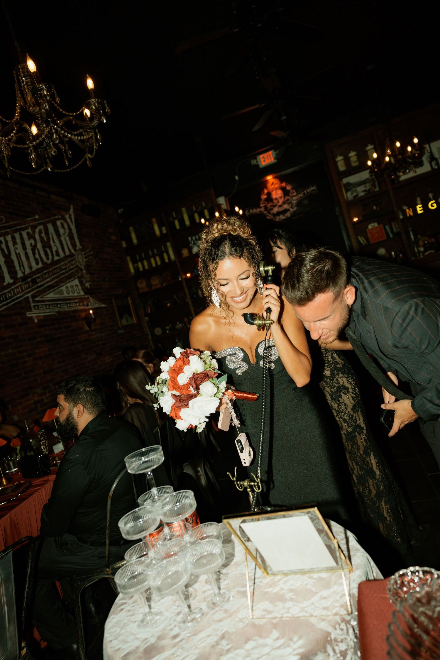 Bride in black gown holds bouquet while groom leans in at elegant dark reception venue.