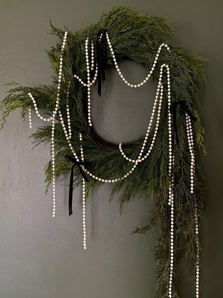 Elegant Christmas wreath made of fresh cedar branches adorned with pearl garlands and black velvet ribbons.