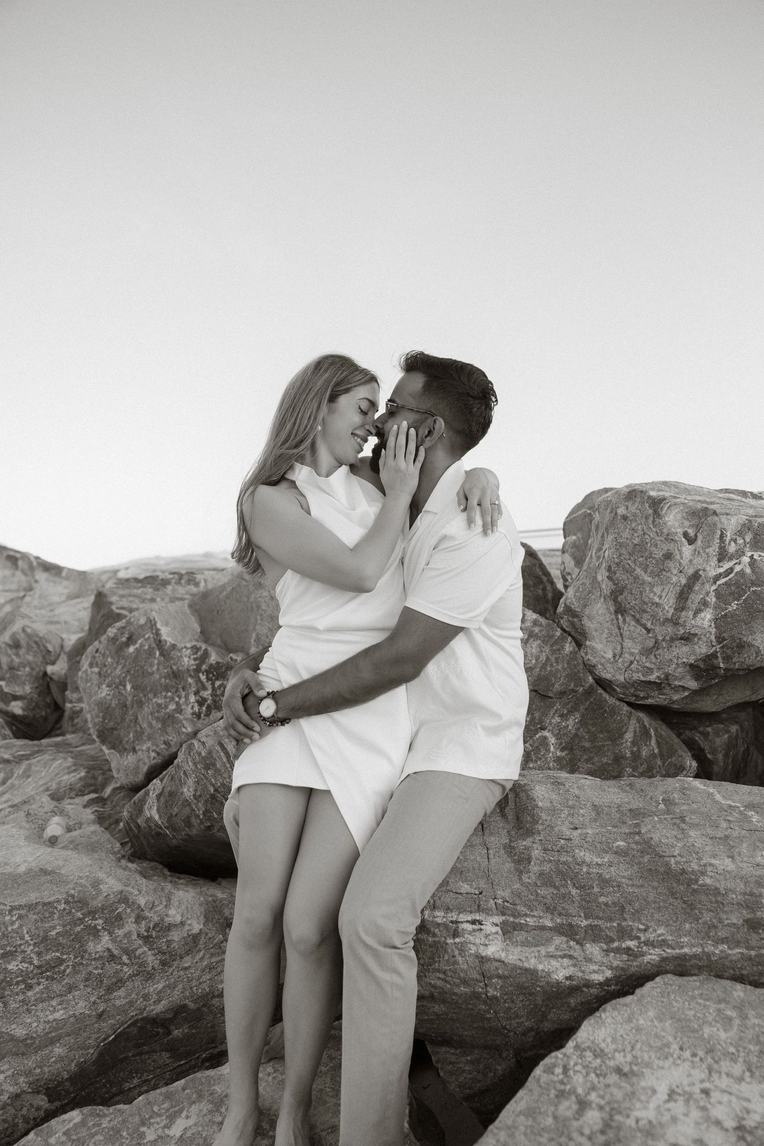 Romantic black and white portrait of a couple embracing on rocky terrain with a minimalist background.