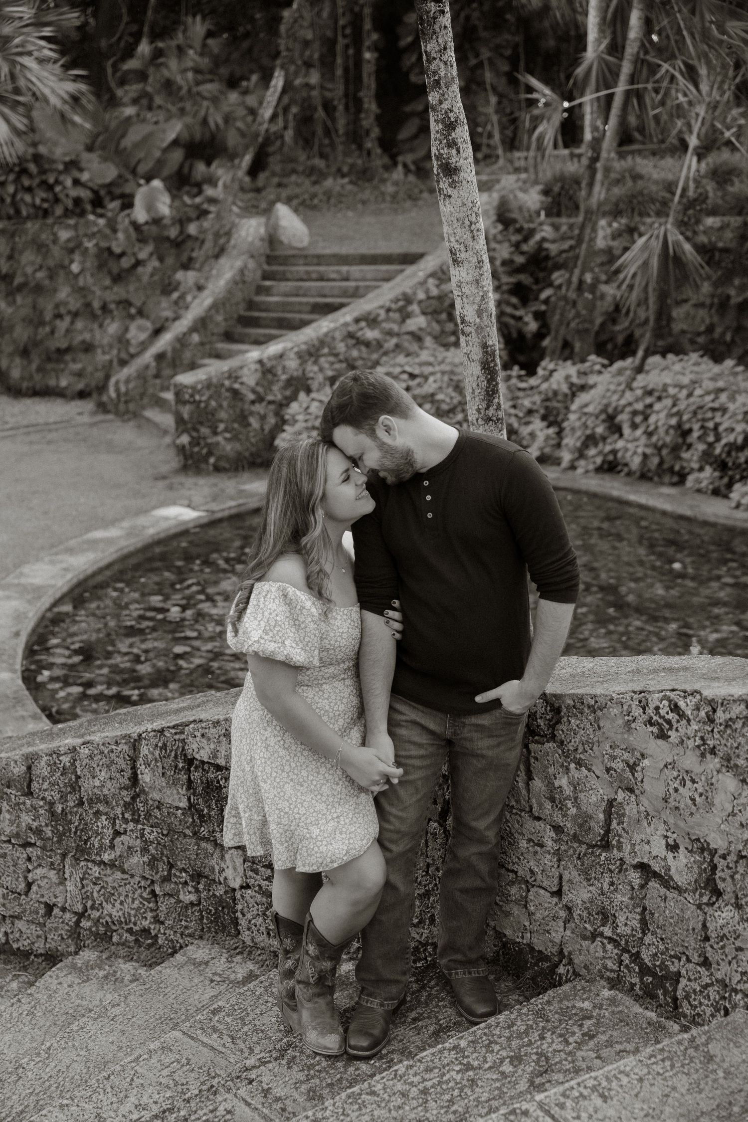 Romantic black and white photo of a couple sharing an intimate moment on stone steps in a garden setting.