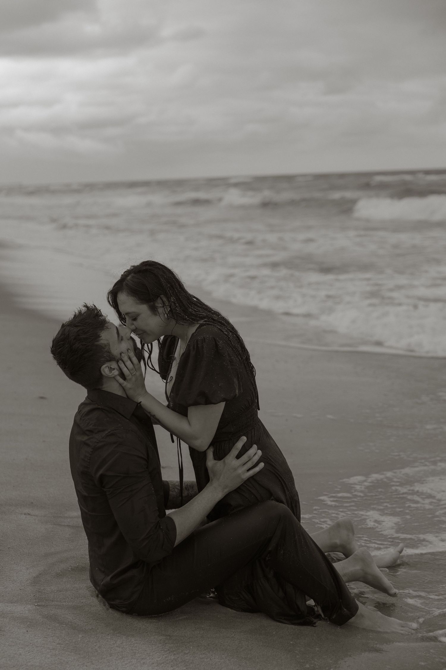 A romantic black and white photo series shows a couple embracing on a misty beach shoreline.