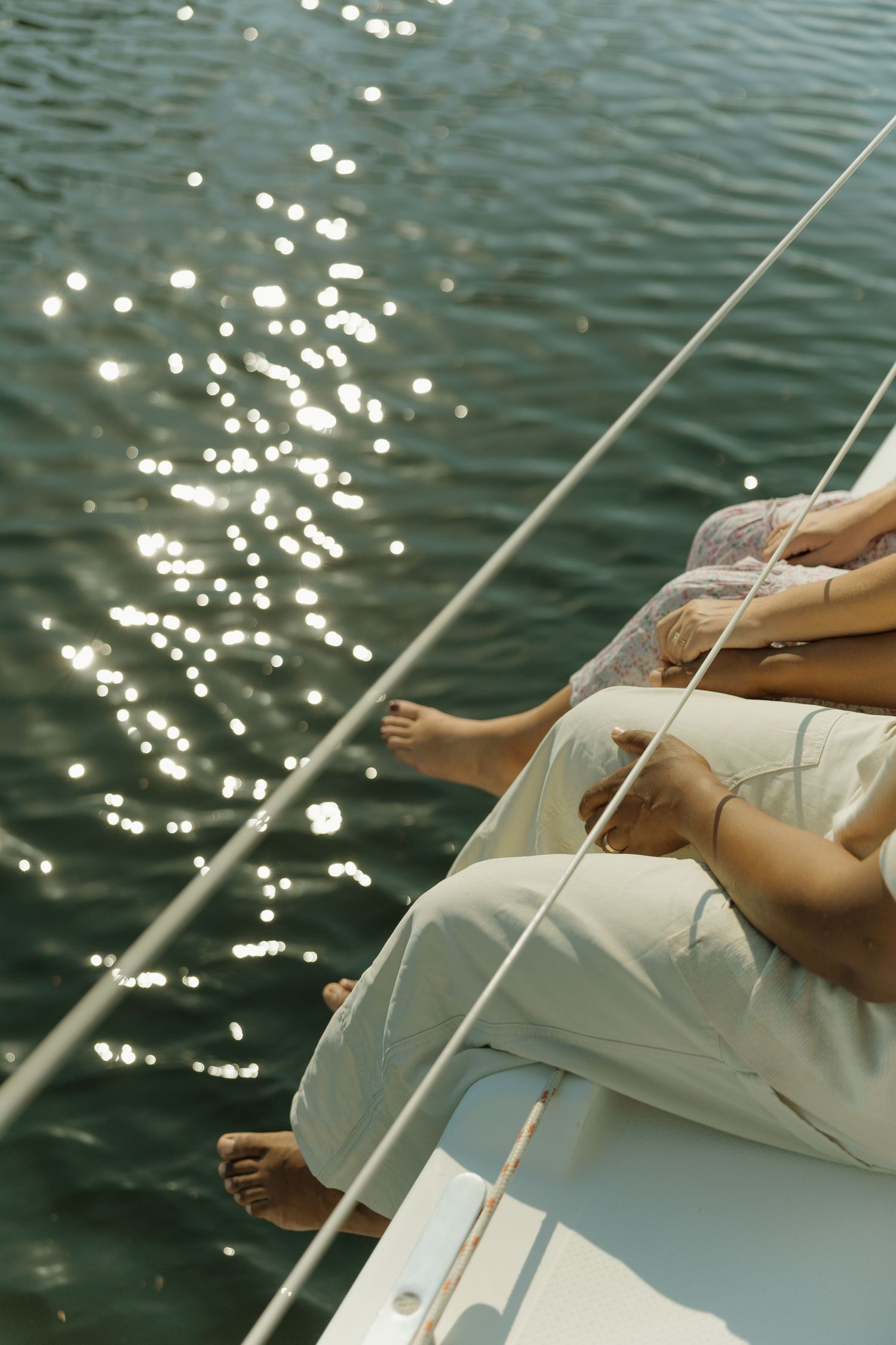 People relaxing on the bow of a sailboat with bare feet dangling over sparkling water on a sunny day.