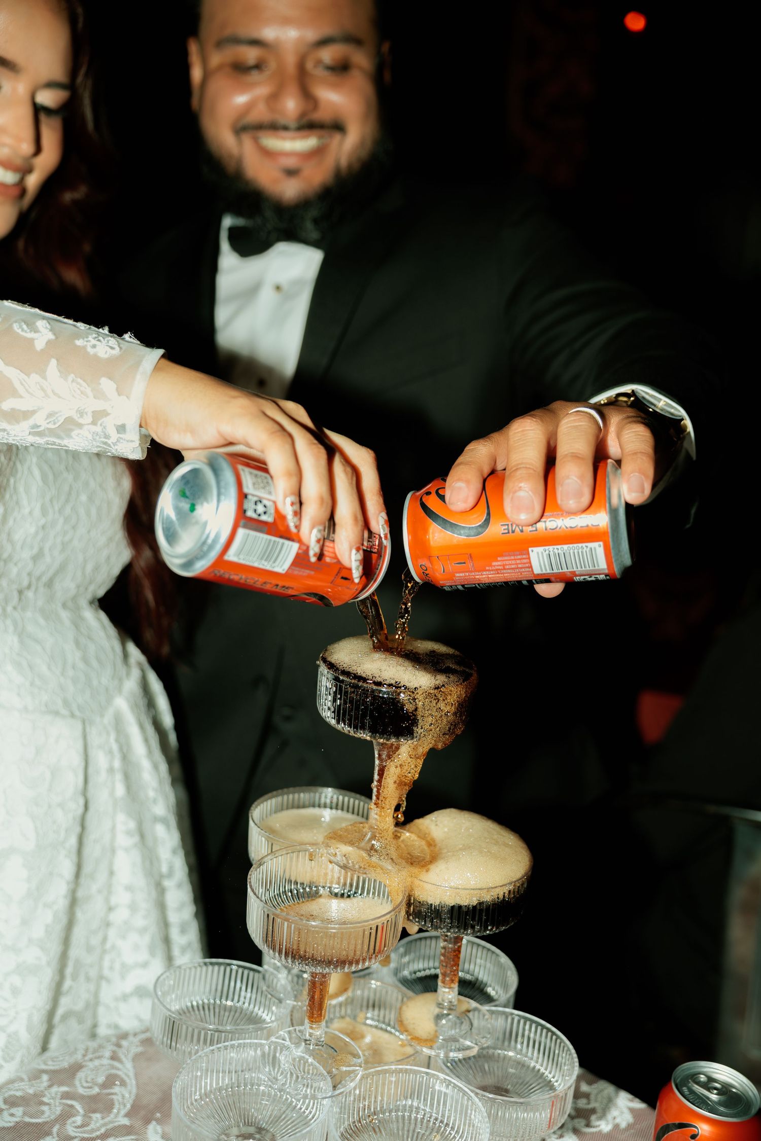 Bride and groom pouring orange soda cans into a champagne tower at their wedding reception.