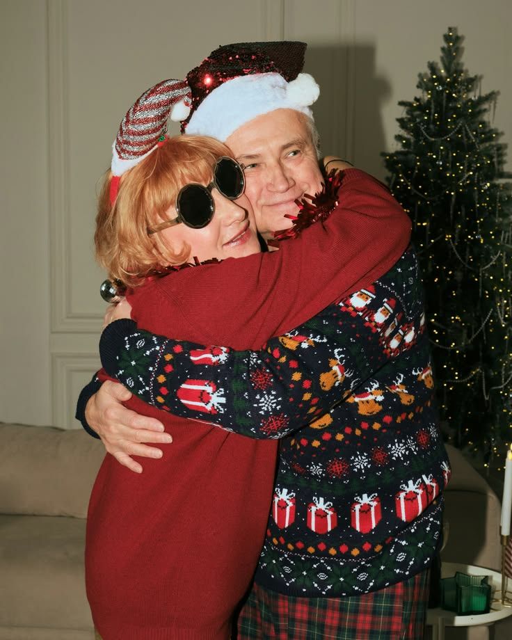 Two people hugging in Christmas sweaters and Santa hats near a decorated Christmas tree.