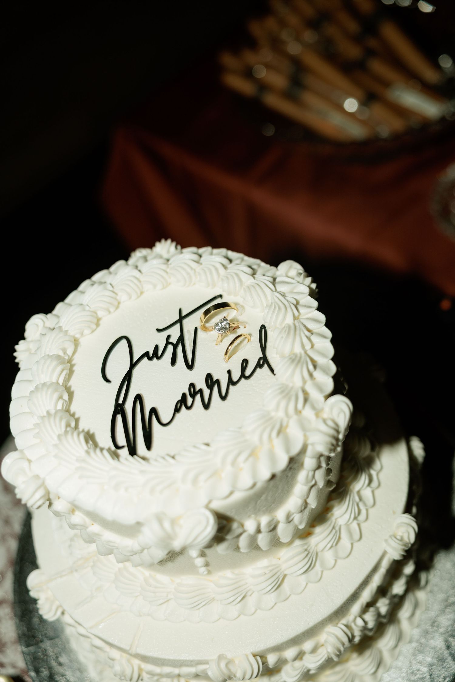 White two-tier wedding cake with Just Married script topper and wedding rings on elegant white frosting decorations.