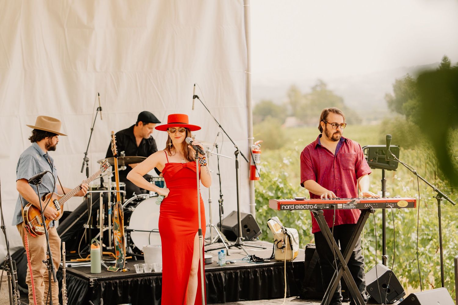 Live band performs on an outdoor stage with musicians playing instruments in warm sunlight.