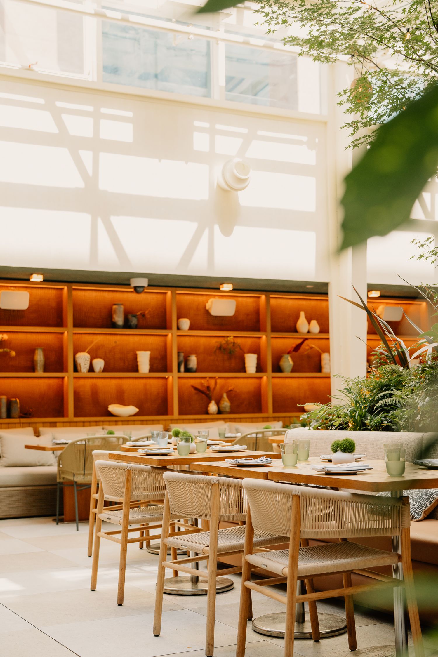 Modern restaurant interior with wooden chairs and tables against wall of terracotta shelving displaying ceramic pottery.