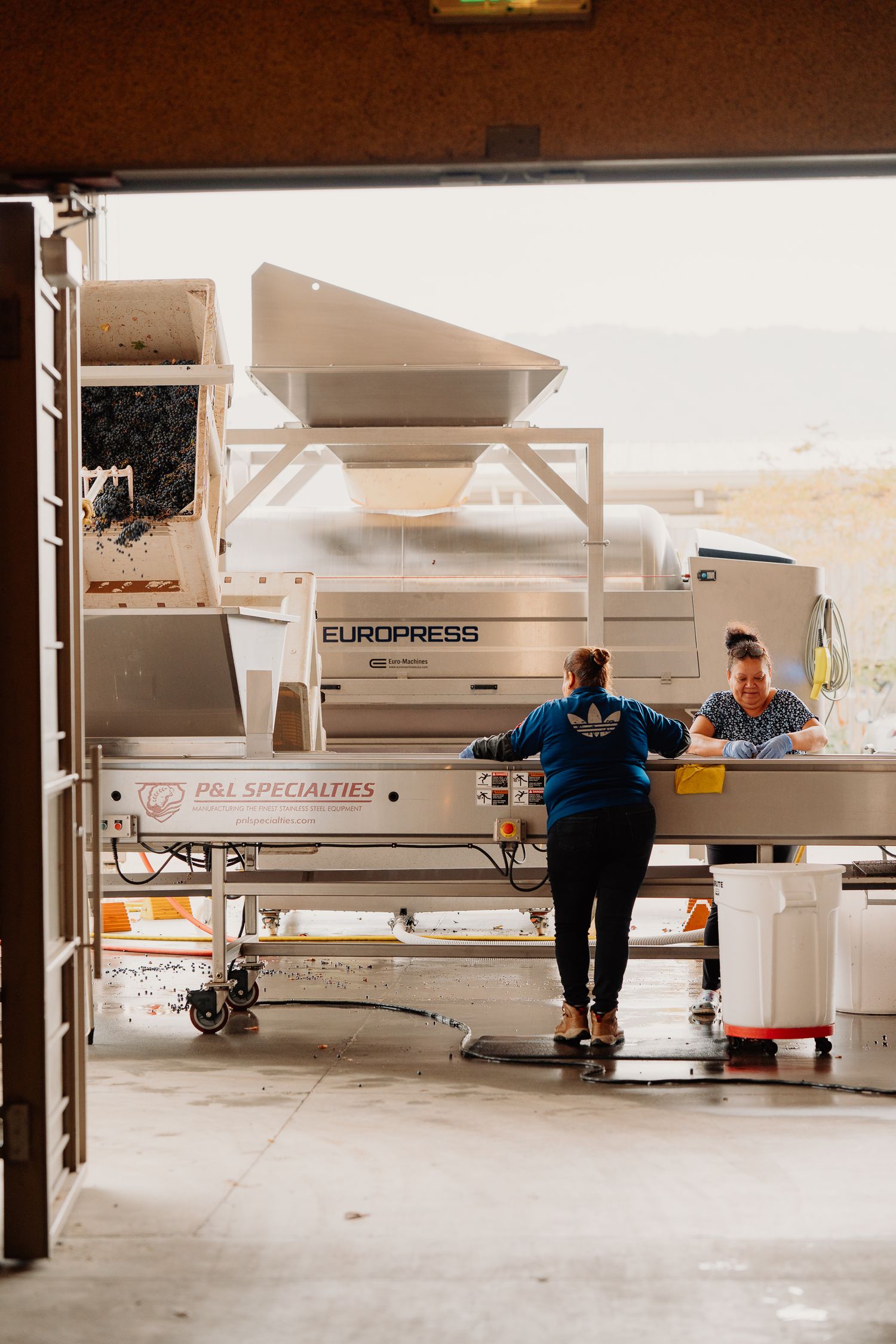 Two women working at a Europress wine processing station inside a winery facility during harvest season.