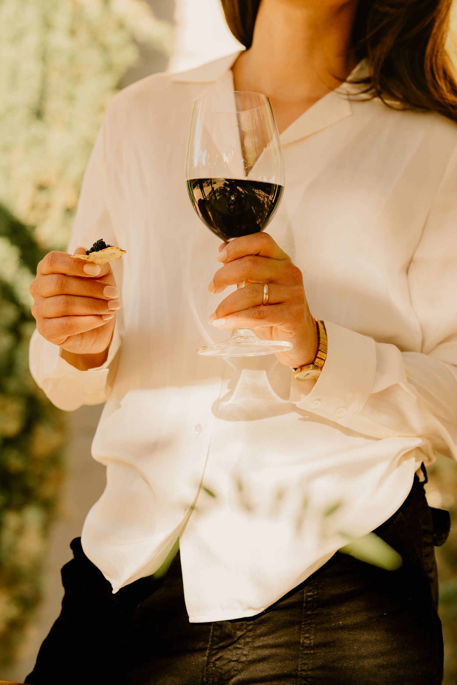 Woman in white blouse holding wine glass and caviar cracker at sunny outdoor wine tasting.