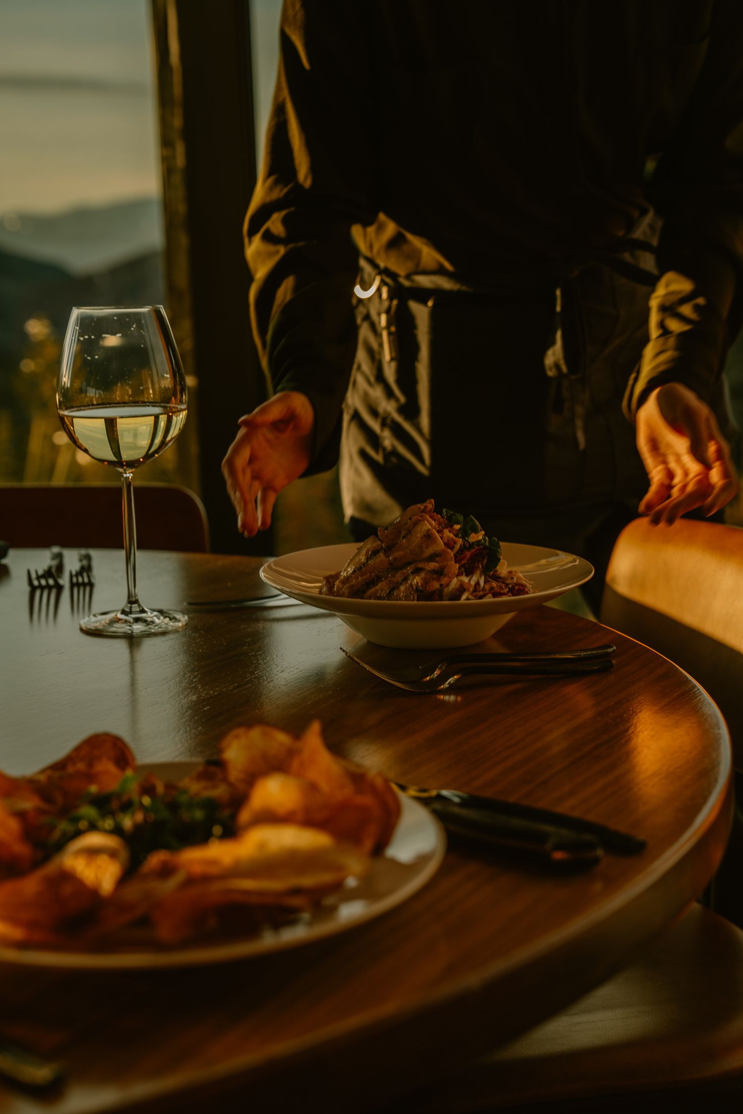 Intimate dinner setting with wine glasses and plates on dark wooden table in dim lighting.