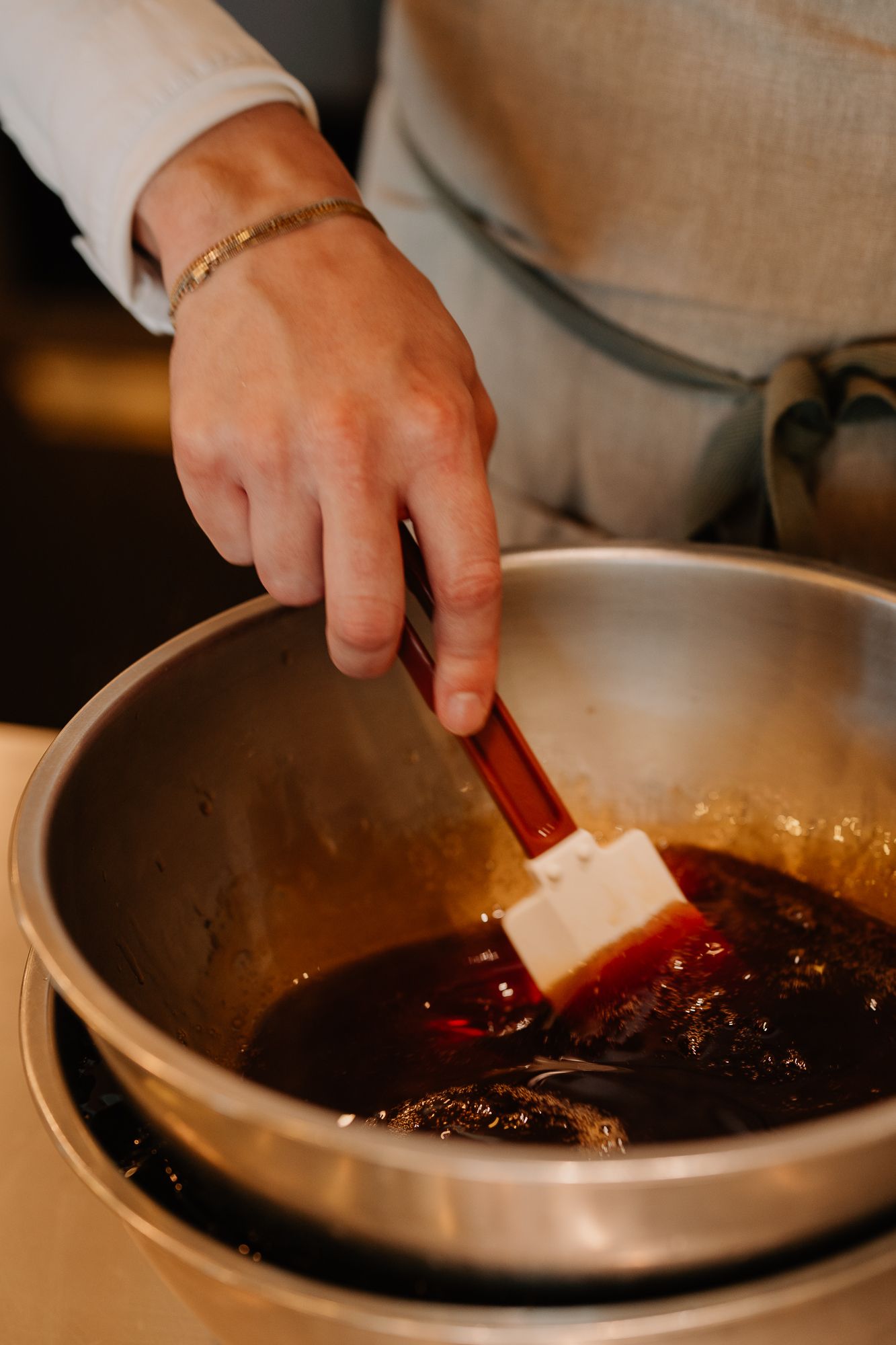 Chef's hand stirring dark red sauce in stainless steel bowl.
