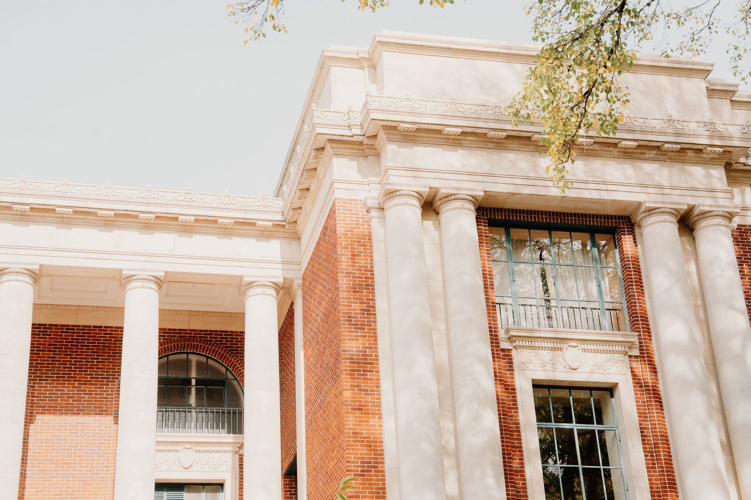 Architectural detail of a historic brick building with white columns and tall windows in warm sunlight.