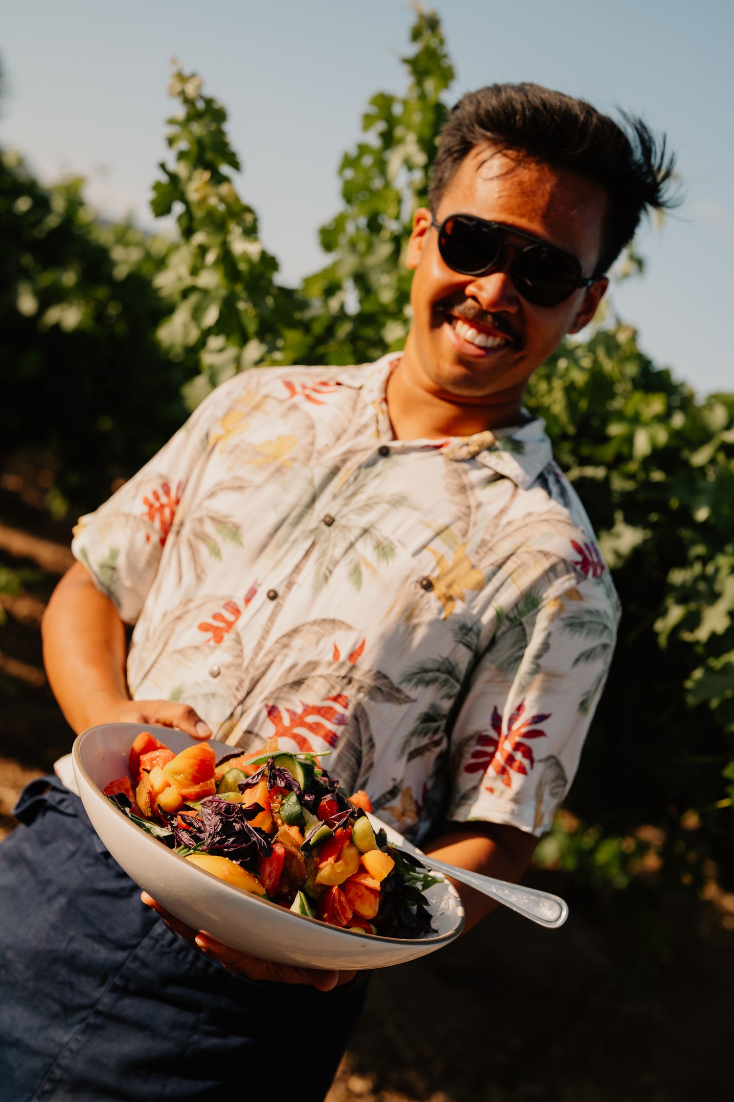 Guest holding colorful salad bowl smiles while enjoying outdoor vineyard dining.