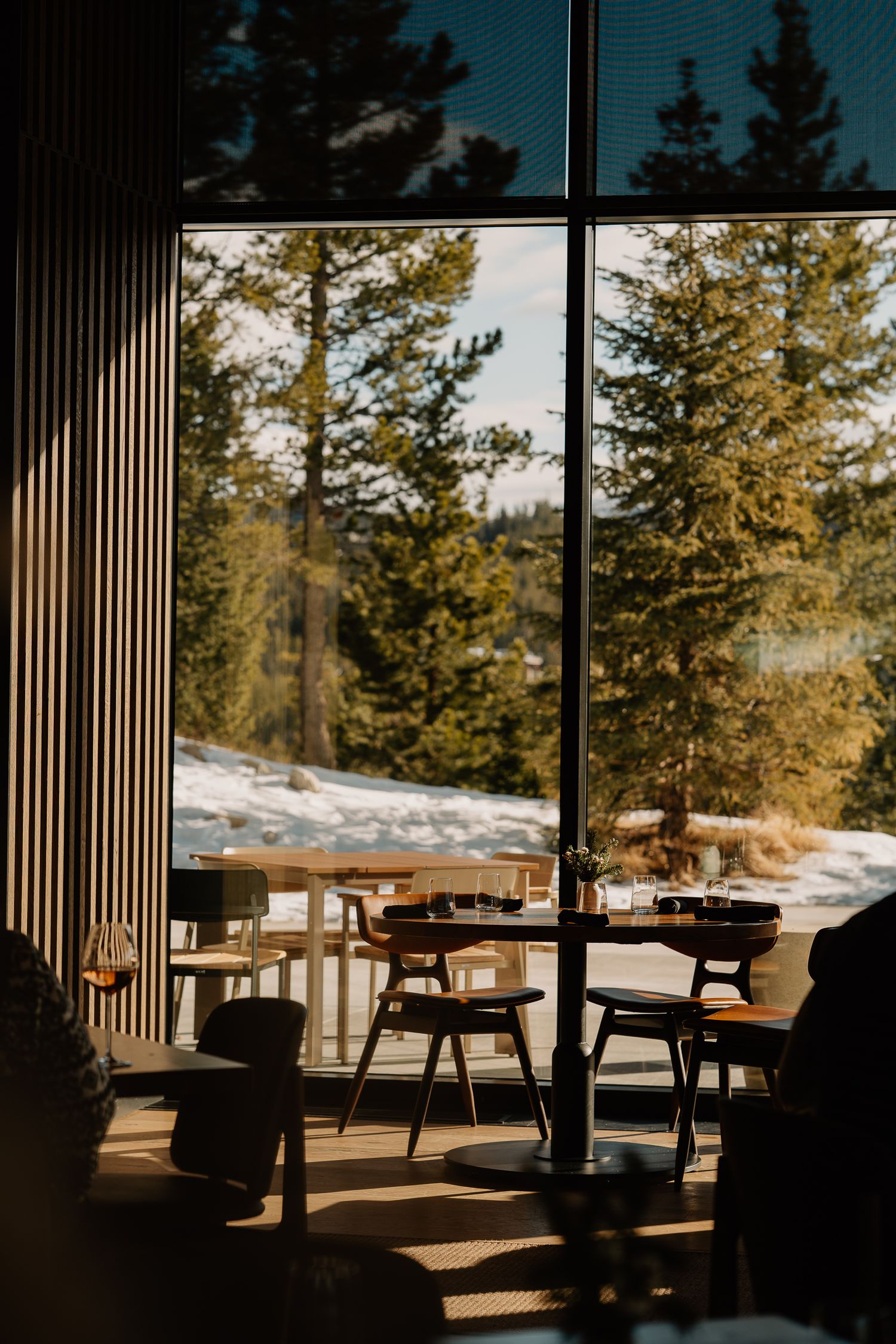 Modern restaurant interior with large windows overlooking a snowy forest landscape.