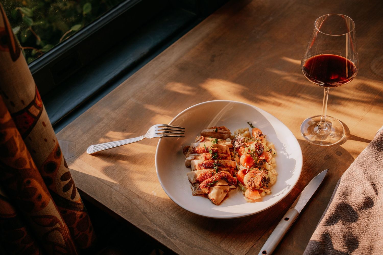 Sunlit restaurant table with white plates and glassware against a dark background.