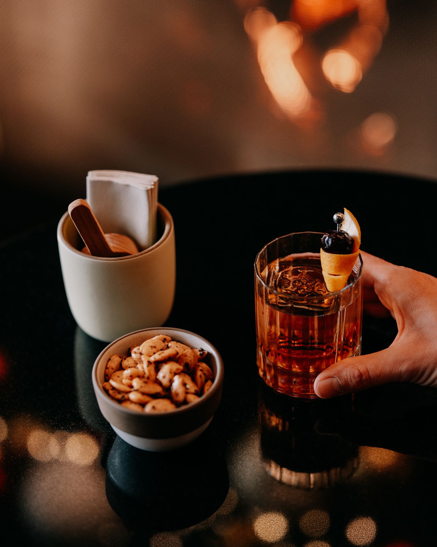 A bowl of mixed nuts and glass of whiskey captured in moody lighting with warm bokeh effects in the background.