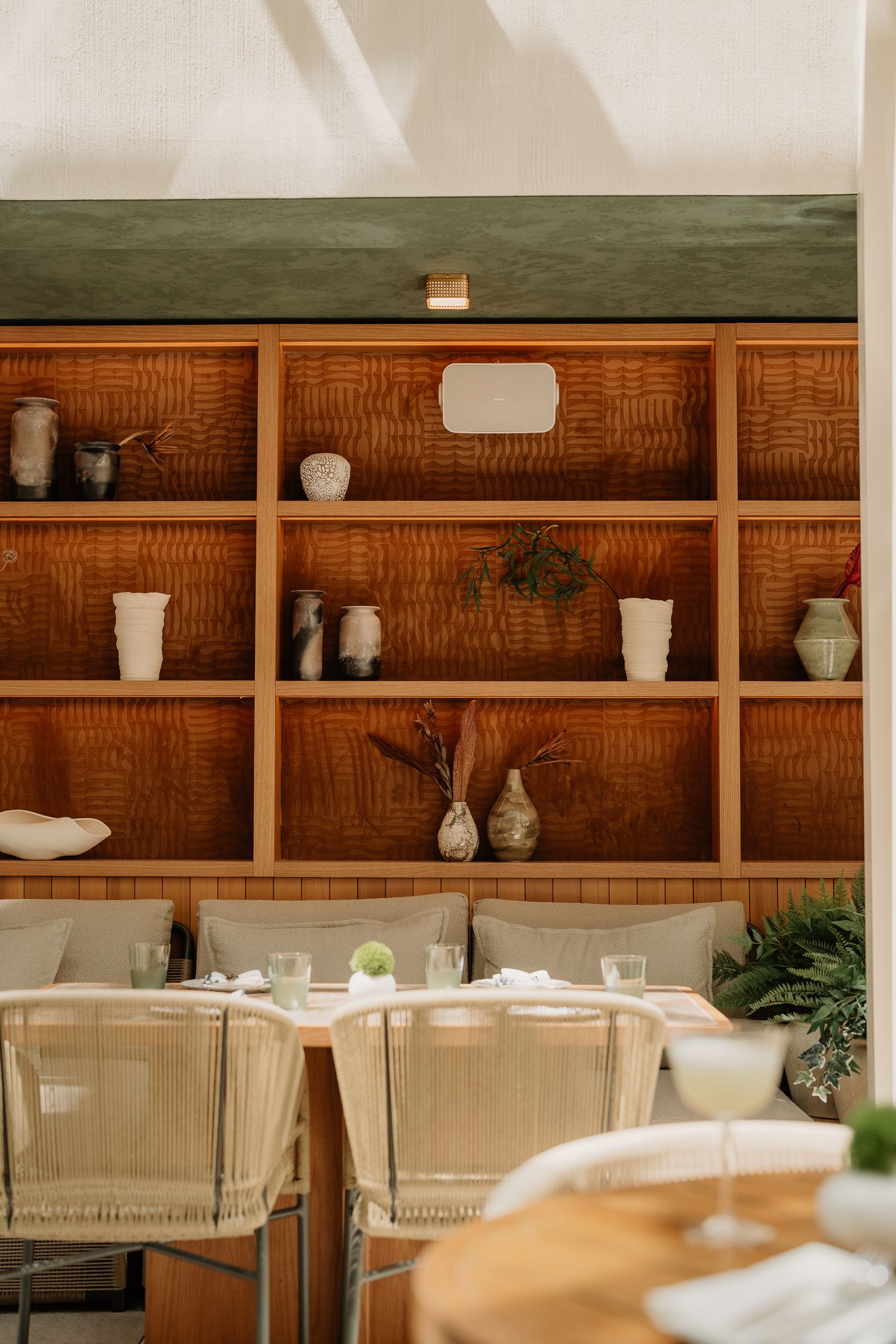 Minimalist dining room features wooden shelving with ceramic vases against a white wall in warm lighting.
