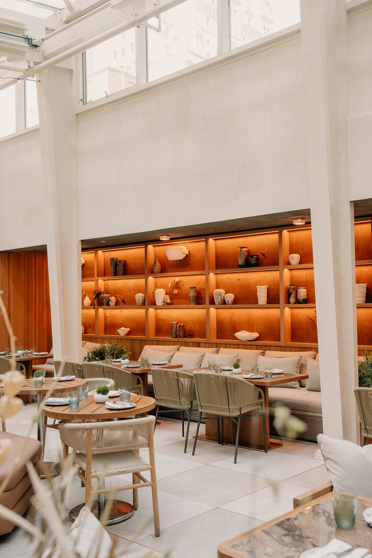 Modern bright restaurant interior with white columns and warm wood banquette seating along illuminated walls.