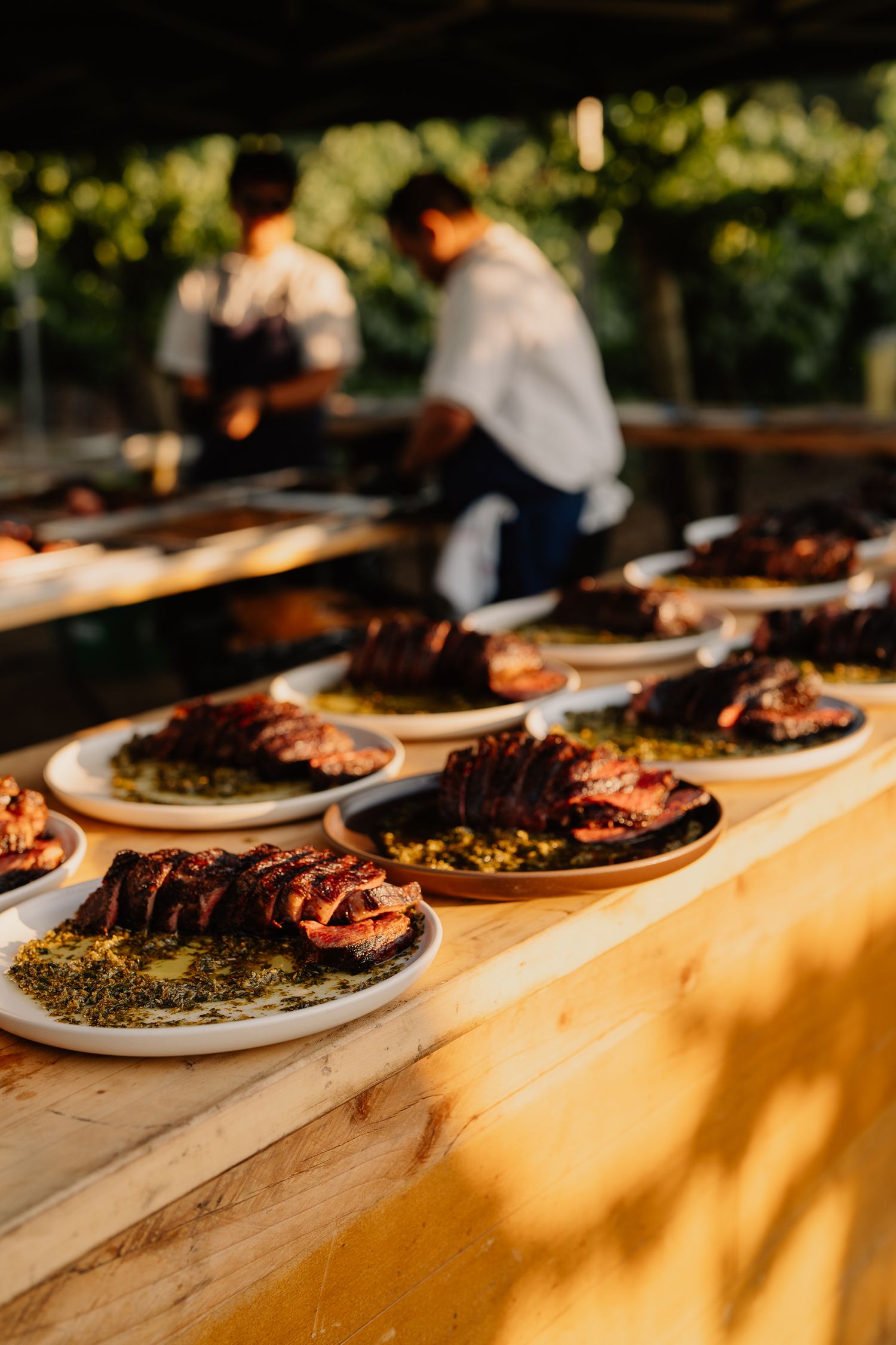Row of plated grilled meats on white dishes at sunset outdoor dining setup.