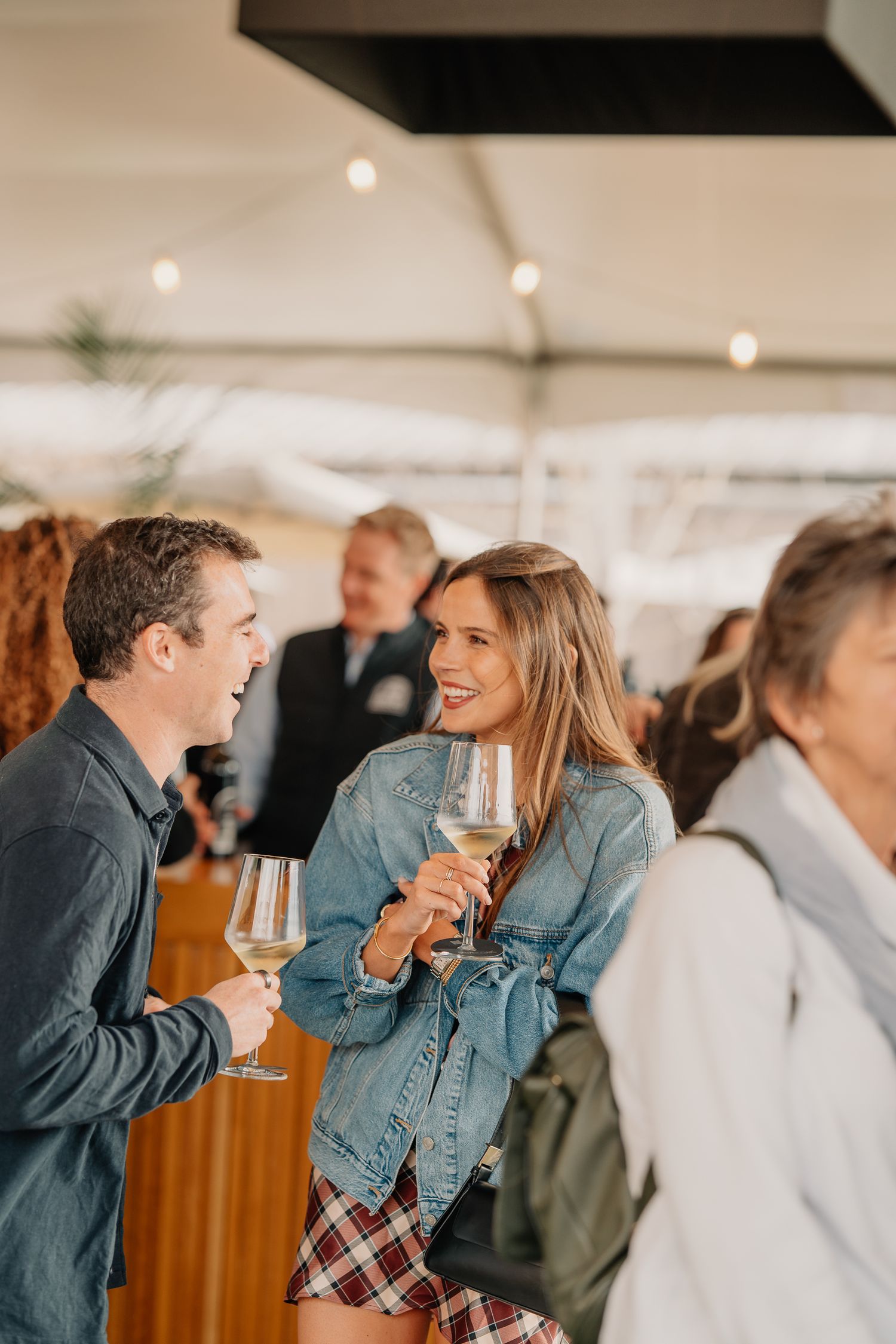 Couple laughing and clinking white wine glasses at a Silver Oak winery tasting event under a tent.