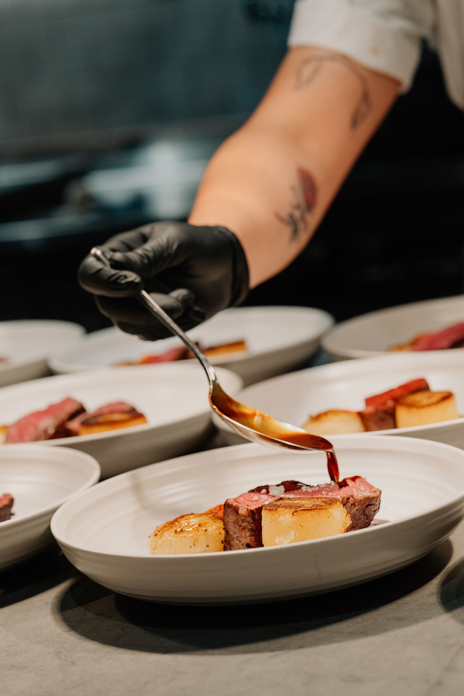 Chef in black gloves plating elegant dishes with precision on white ceramic plates at an upscale restaurant.