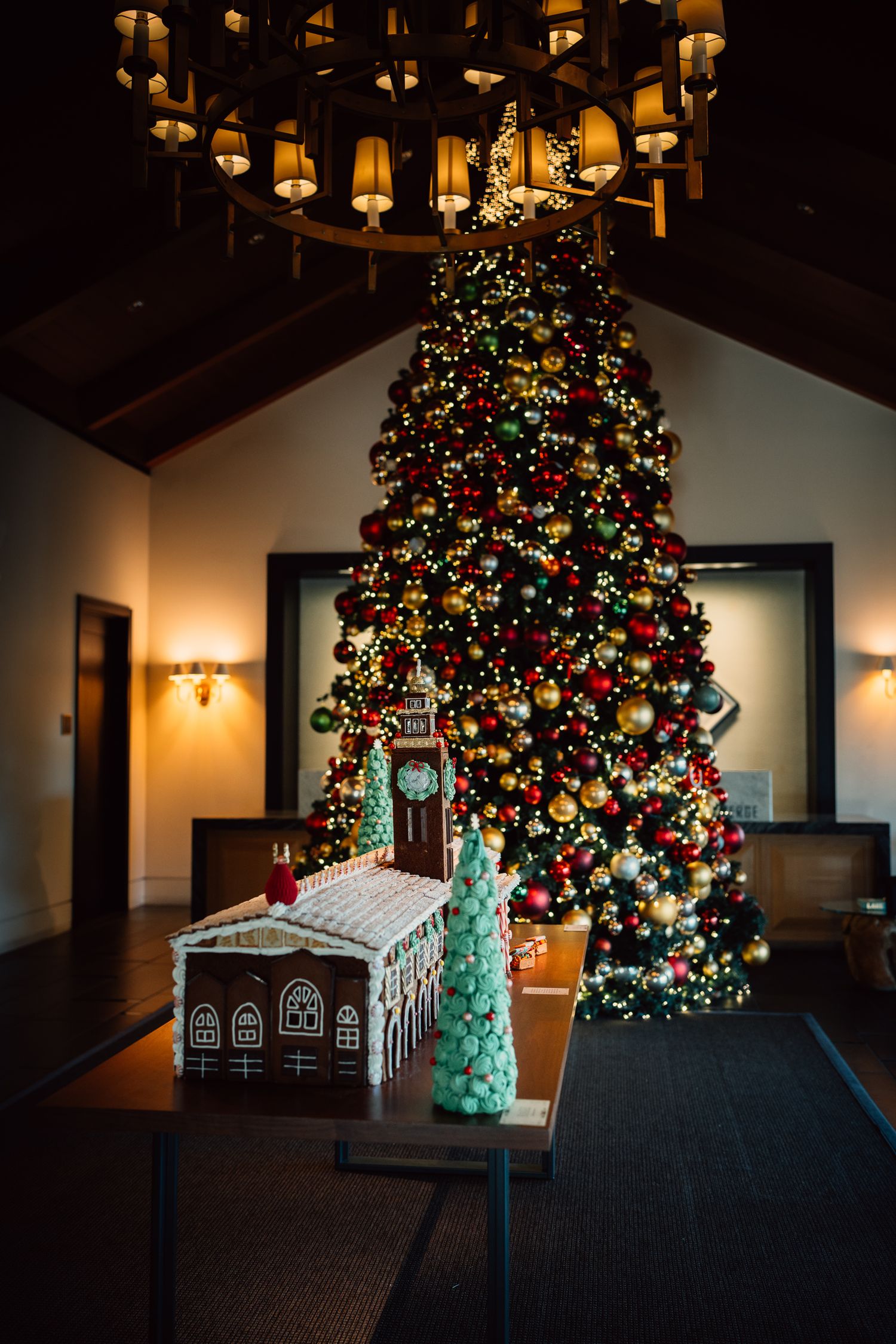 A large decorated Christmas tree and gingerbread house display illuminated in a dark room with warm lighting.