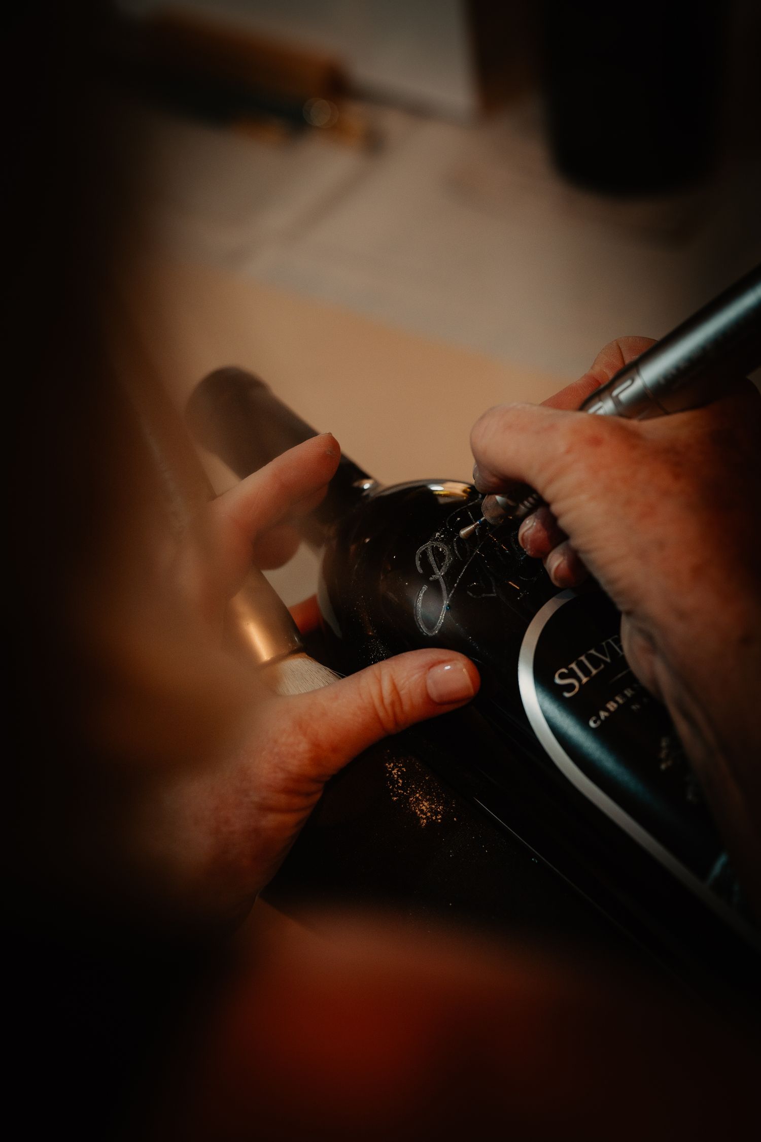 Close-up of hands signing a Silver Oak Cabernet Sauvignon wine bottle with a pen.