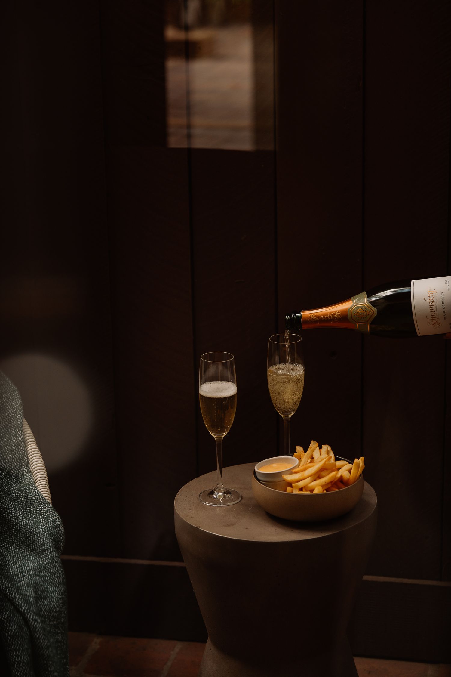 Champagne being poured into elegant flutes beside a bowl of french fries in a dimly lit setting.