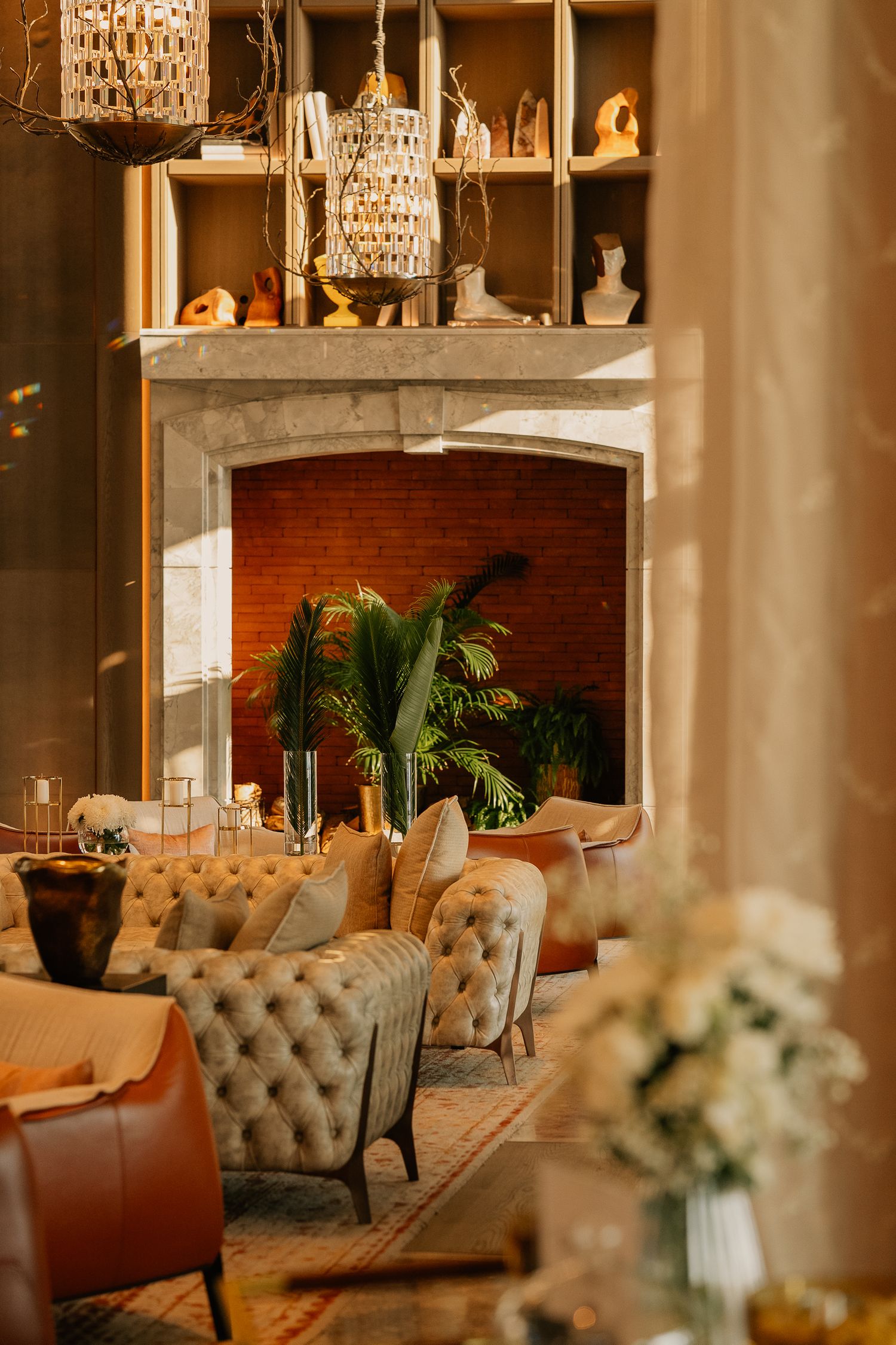 Elegant lounge with tufted sofas, fireplace, crystal chandelier, and lush tropical plants.