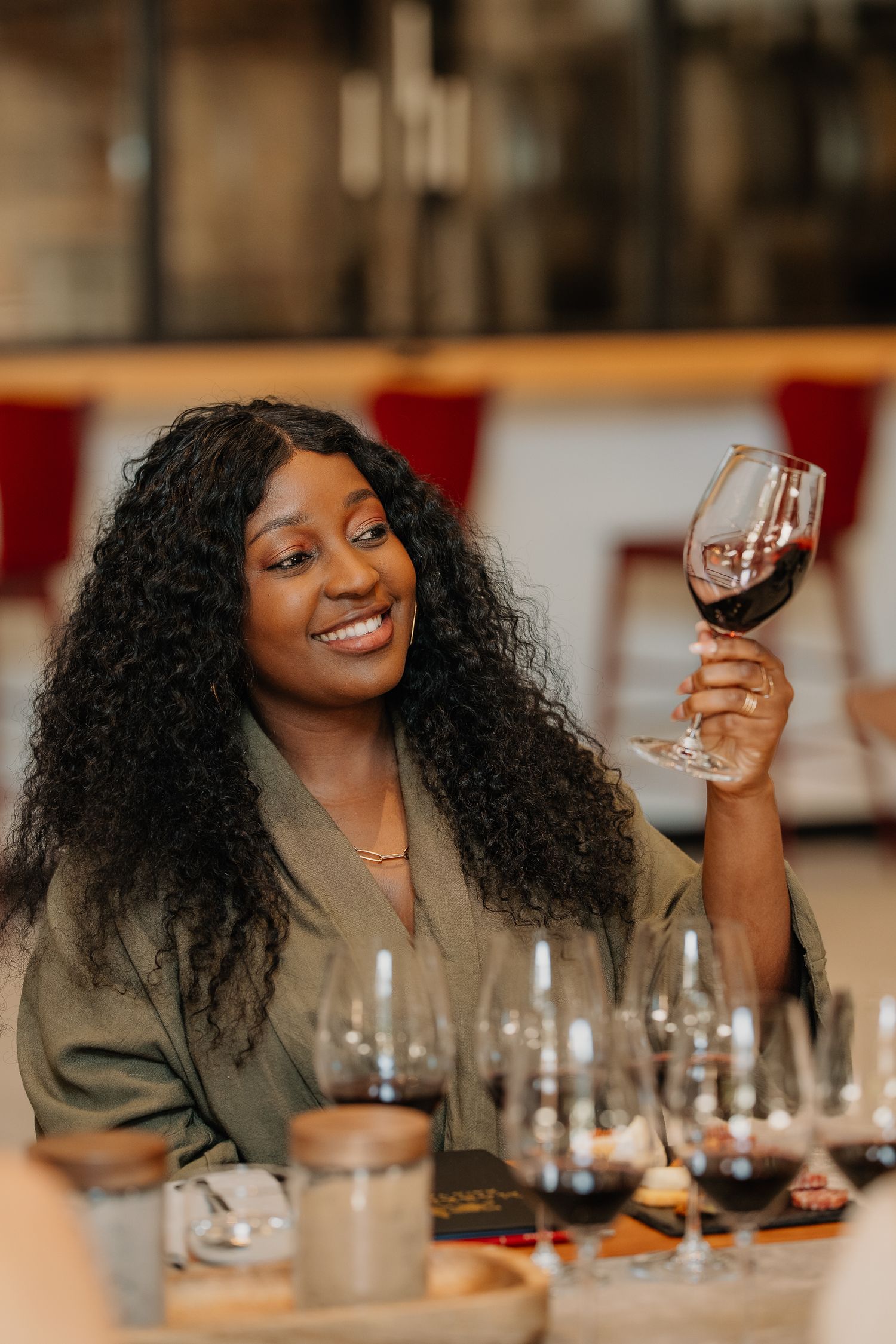 Smiling woman holding a glass of red wine at a wine tasting event in a restaurant.