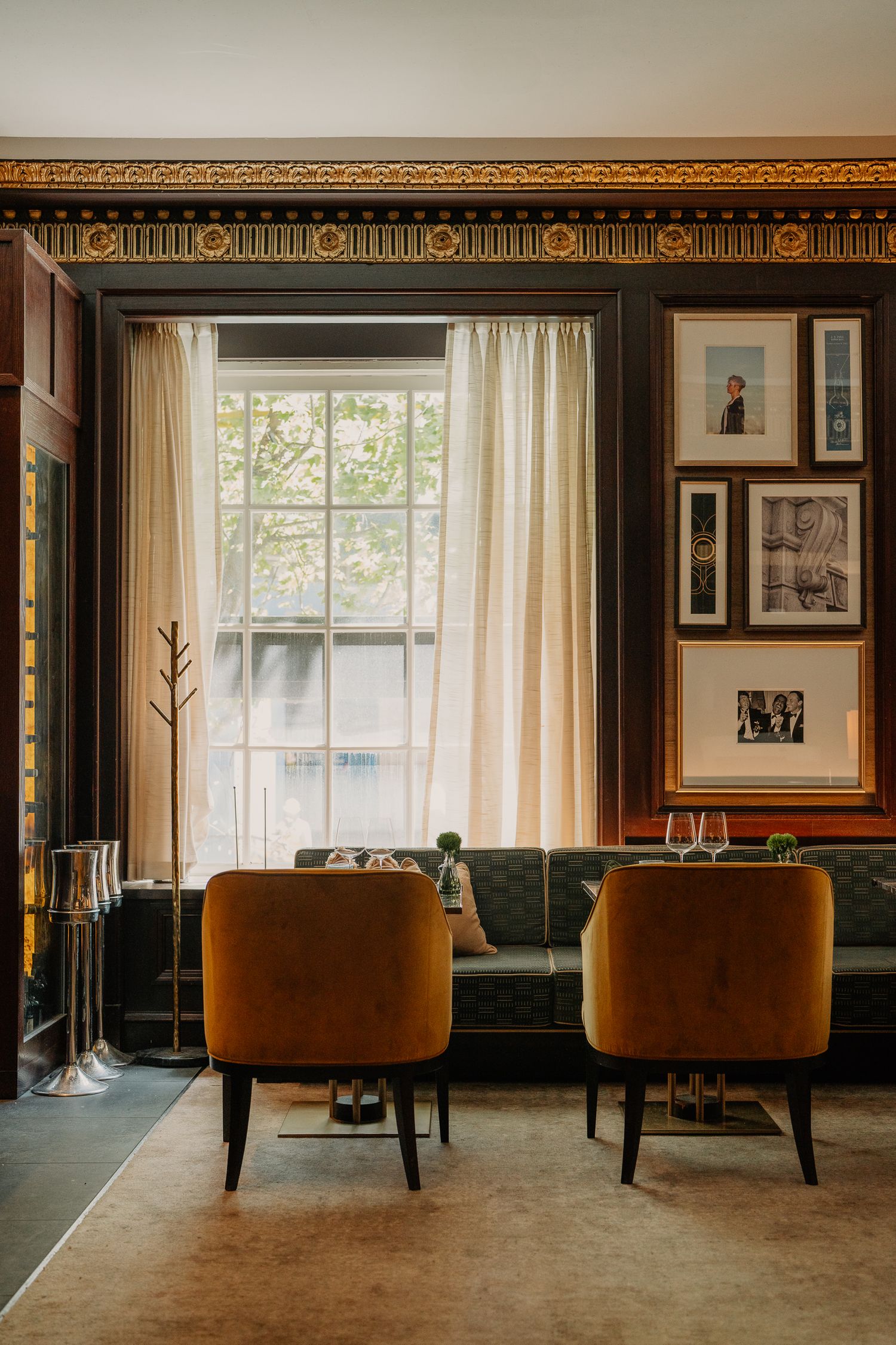 Sophisticated hotel interior with brown leather chairs, framed photographs, and large windows with sheer curtains.