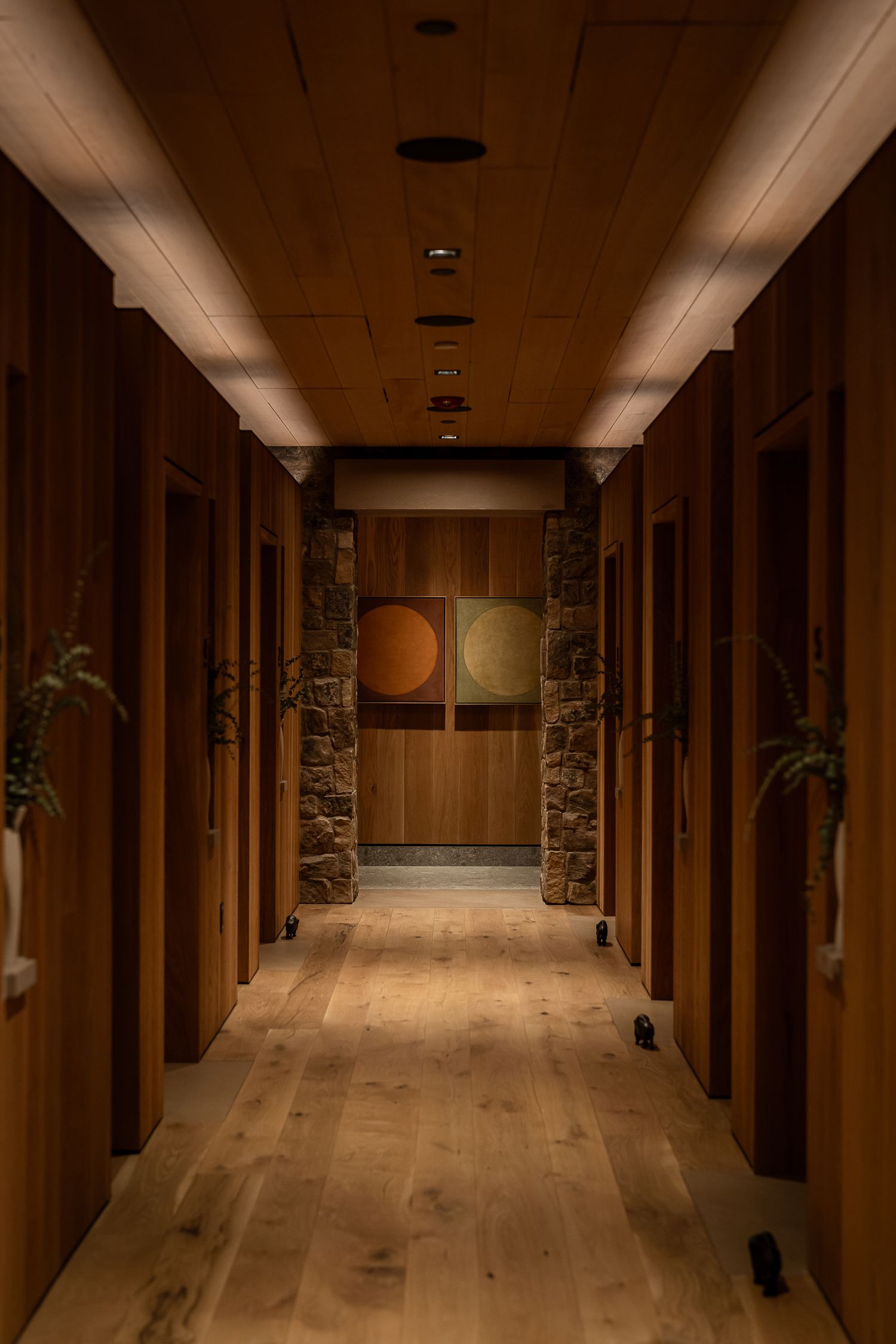 Warm-lit hallway with wood floors, stone accents, and modern artwork in rustic mountain lodge interior.