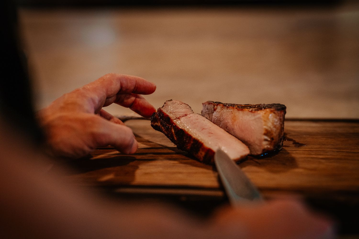 Person slicing a perfectly cooked steak on a wooden cutting board with a sharp knife.