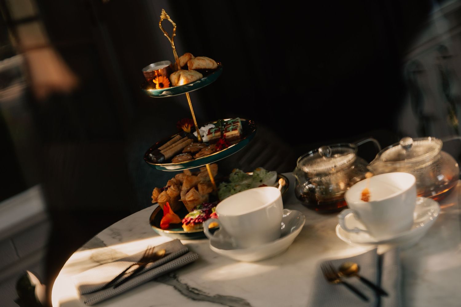 Elegant afternoon tea service with tiered plates of pastries and sandwiches on a white tablecloth in dim lighting.