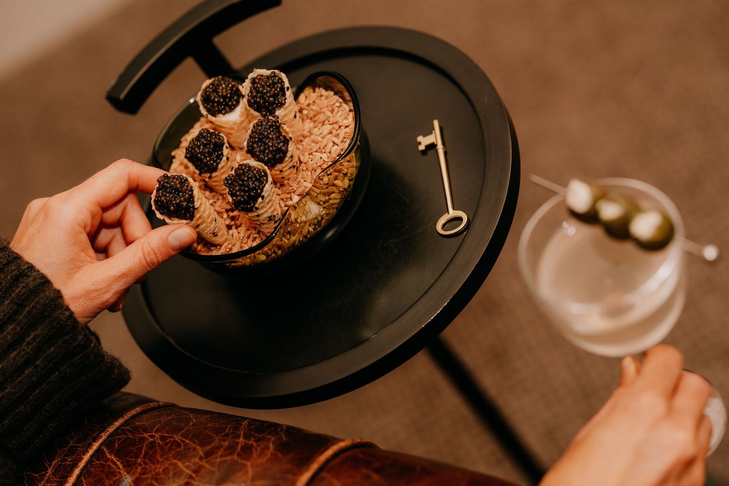 Hands holding plates of chocolate chip cookies and glasses of wine in a cozy restaurant setting.
