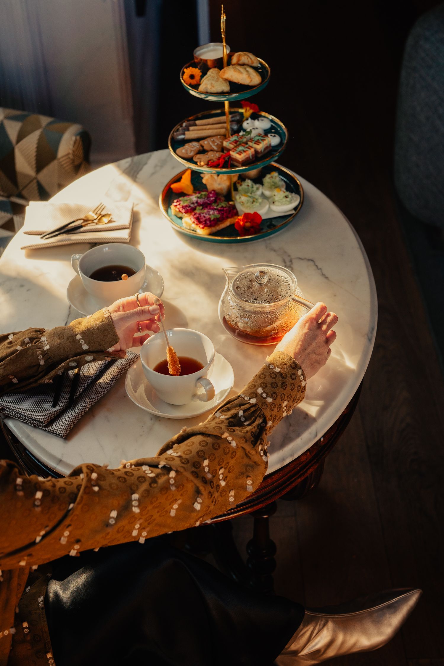 Elegant table setting with tea service and dessert plates on a polished wooden surface in warm lighting.