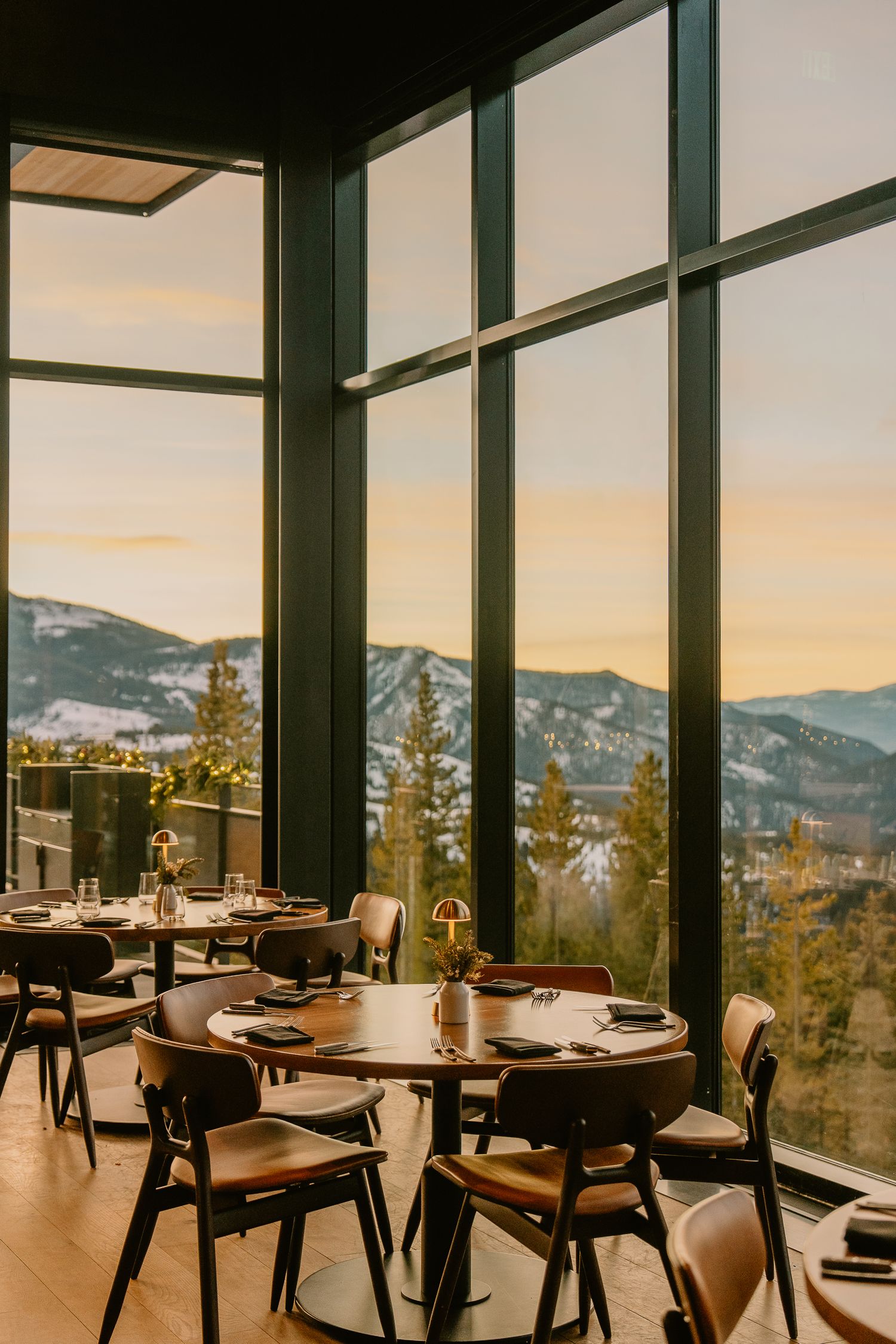 Upscale restaurant dining room with floor-to-ceiling windows offering stunning mountain views at sunset.