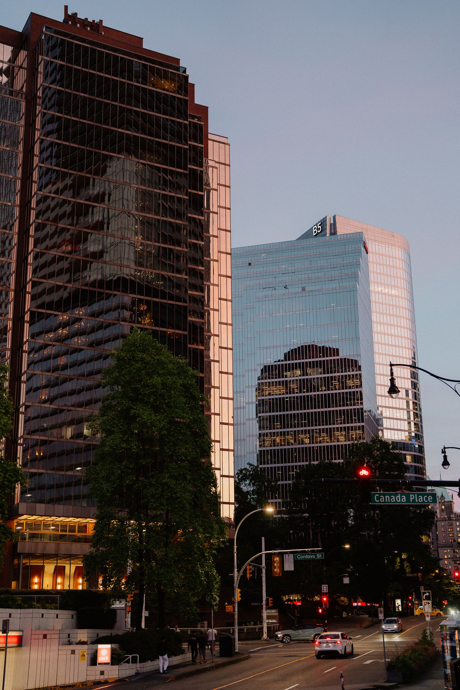 Modern glass skyscrapers reflect sunset light along a city street corner in Vancouver's downtown business district.
