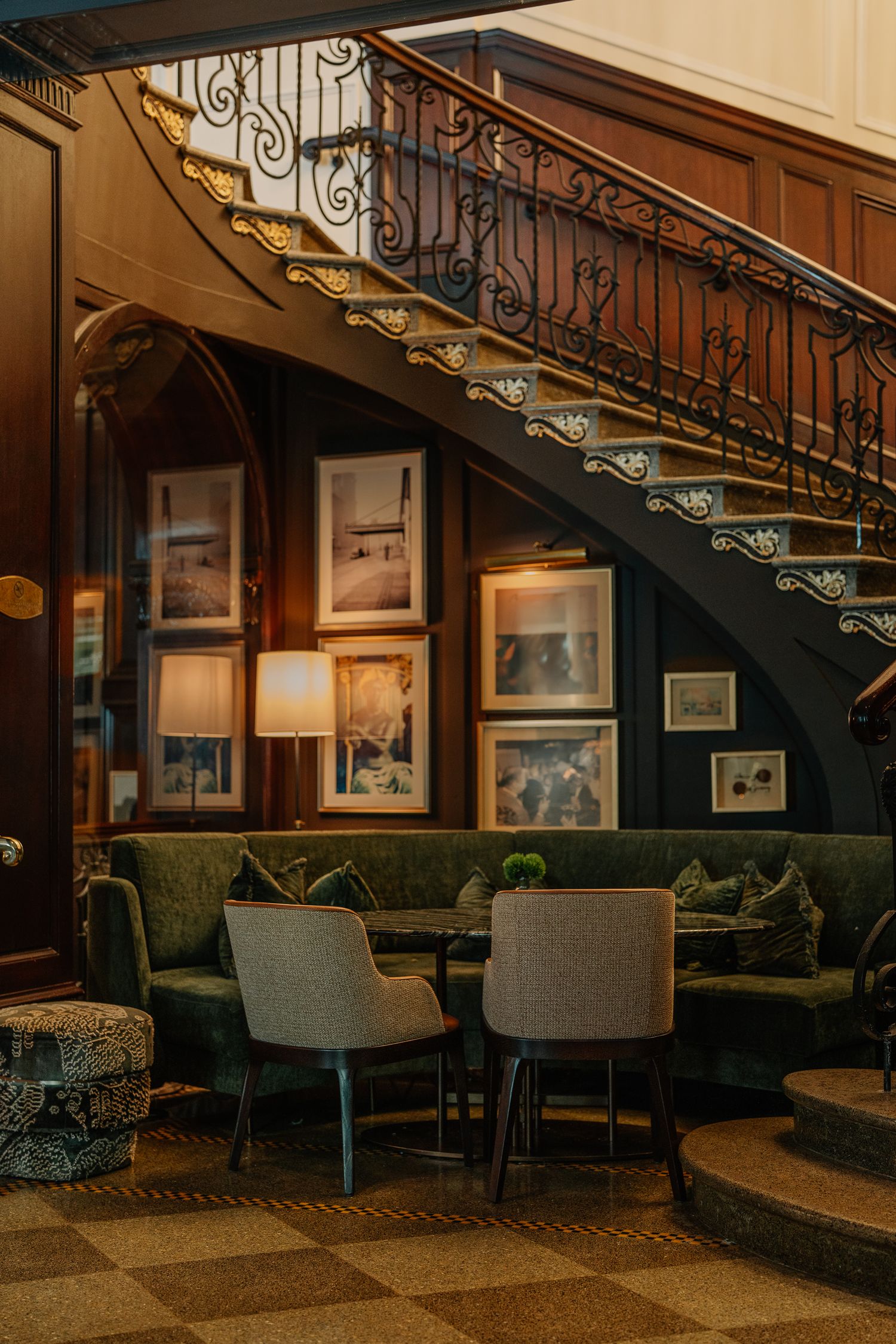 A luxurious lounge area beneath an ornate wooden staircase with framed artwork and upholstered seating.