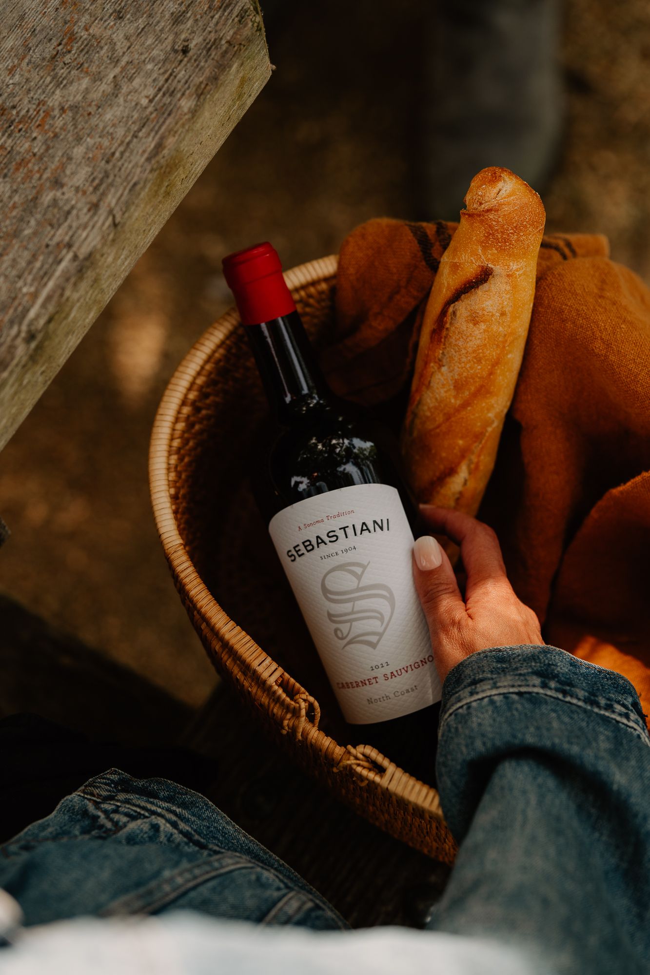 Hand holding a Sebastiani Cabernet Sauvignon wine bottle in a wicker basket with fresh baguettes.