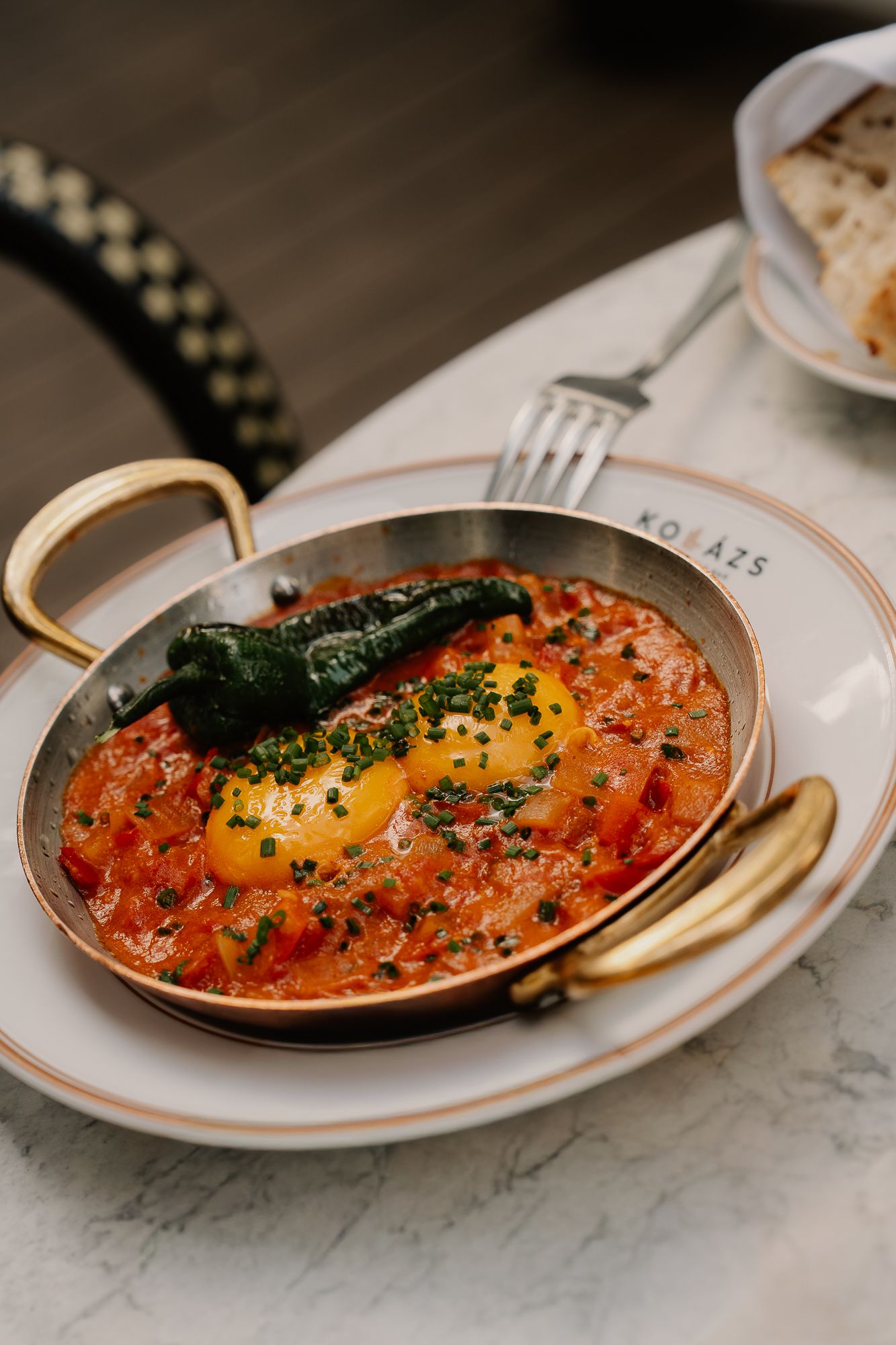 Shakshuka with poached eggs in tomato sauce, topped with herbs and charred pepper, served in a copper pan.