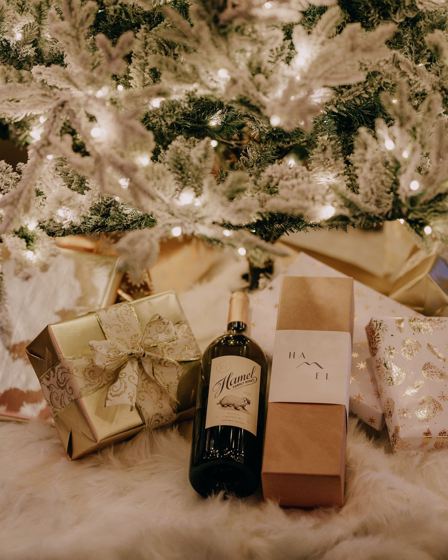 Wrapped Christmas presents and decorative elements arranged under a white frosted Christmas tree in a vintage style setting.