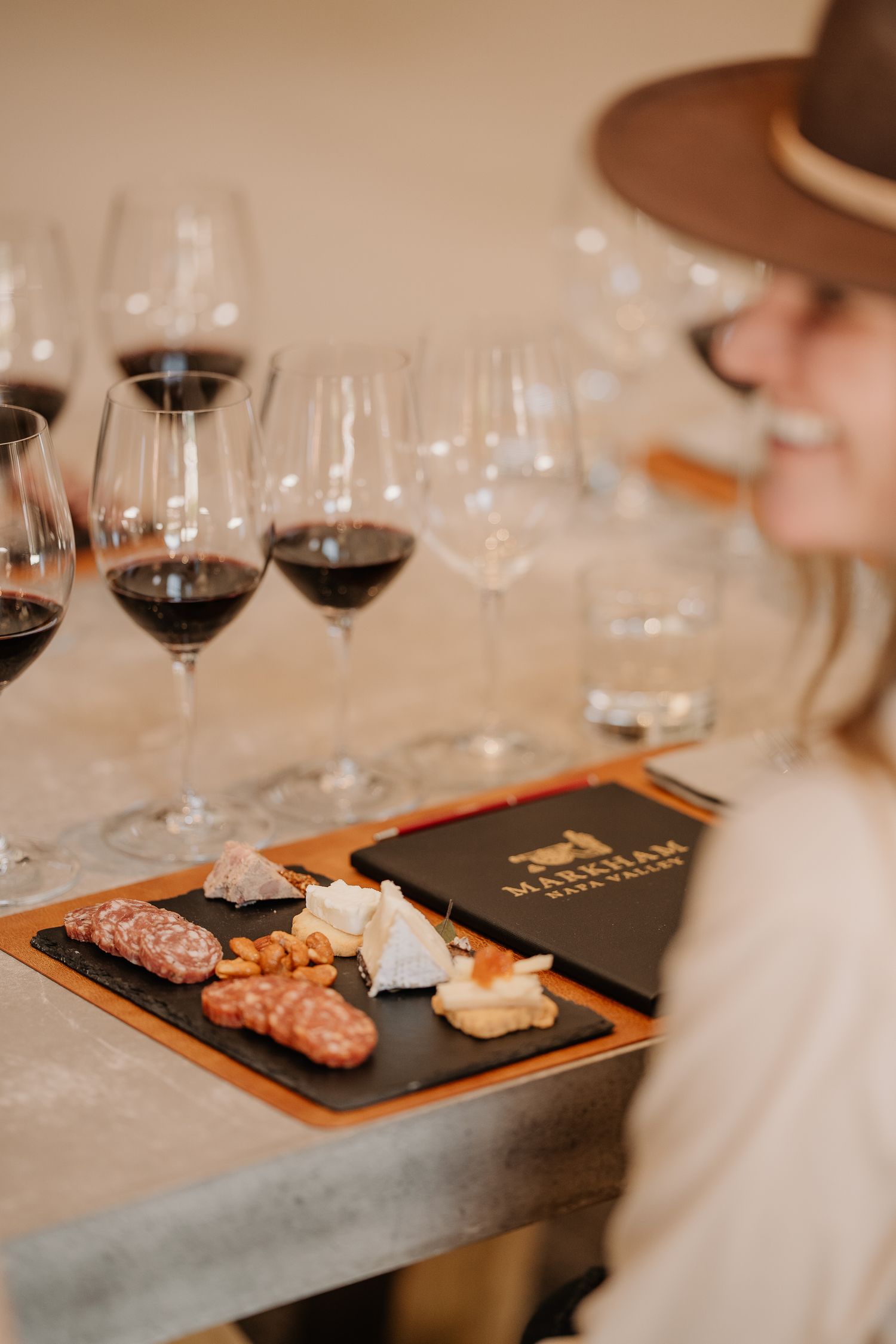 A woman in a hat enjoys a wine tasting with red wines and charcuterie board at Markham Napa Valley.