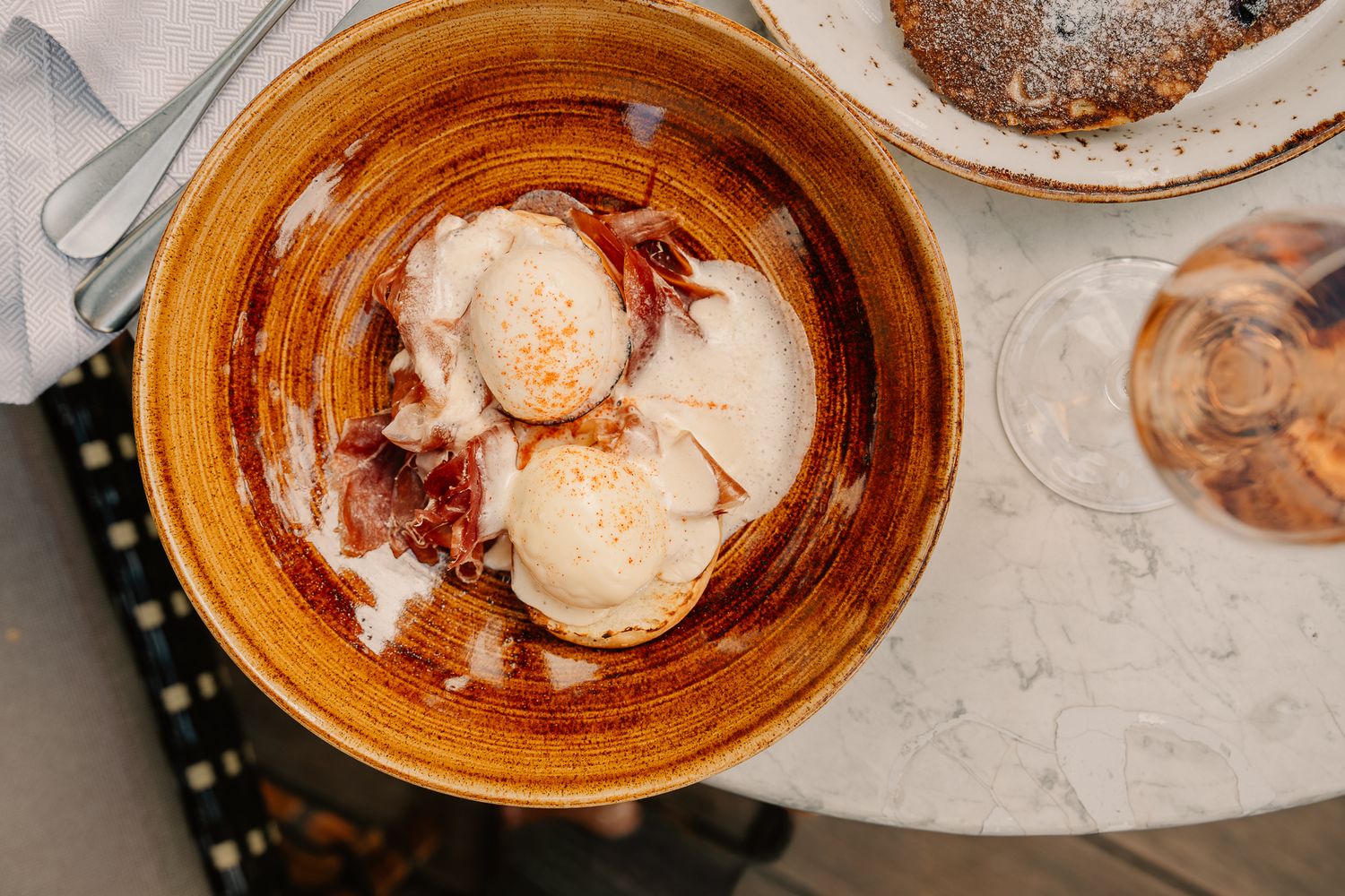 Overhead view of vanilla ice cream scoops in caramel sauce served in a rustic ceramic bowl on marble table.