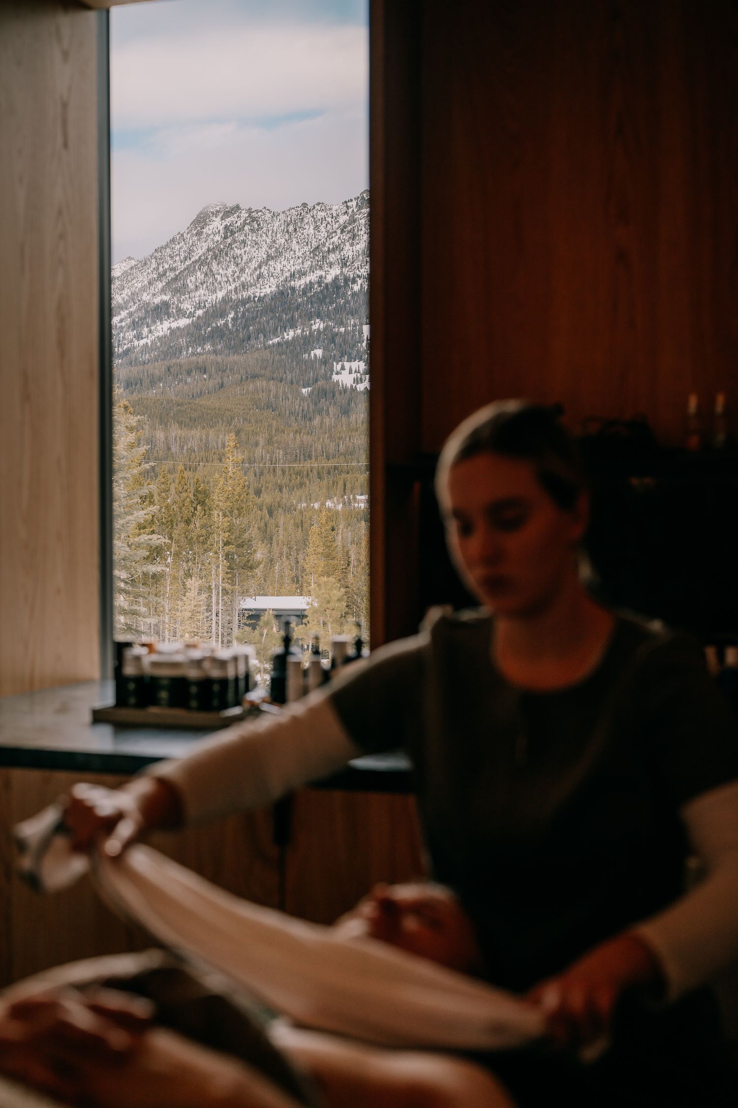Interior view of mountain lodge with snowy peaks visible through large window.