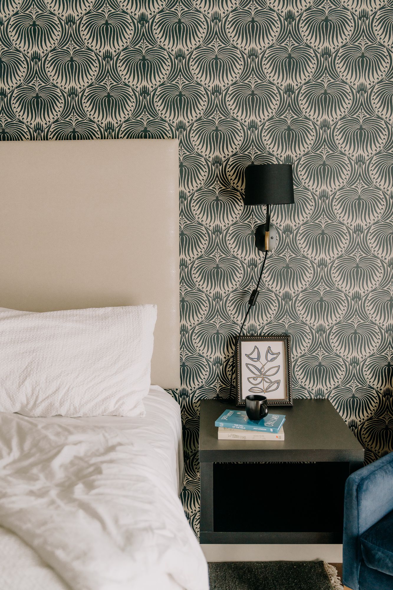 Art deco wallpaper with fan pattern decorates bedroom wall above white bedding and modern sconce lighting.
