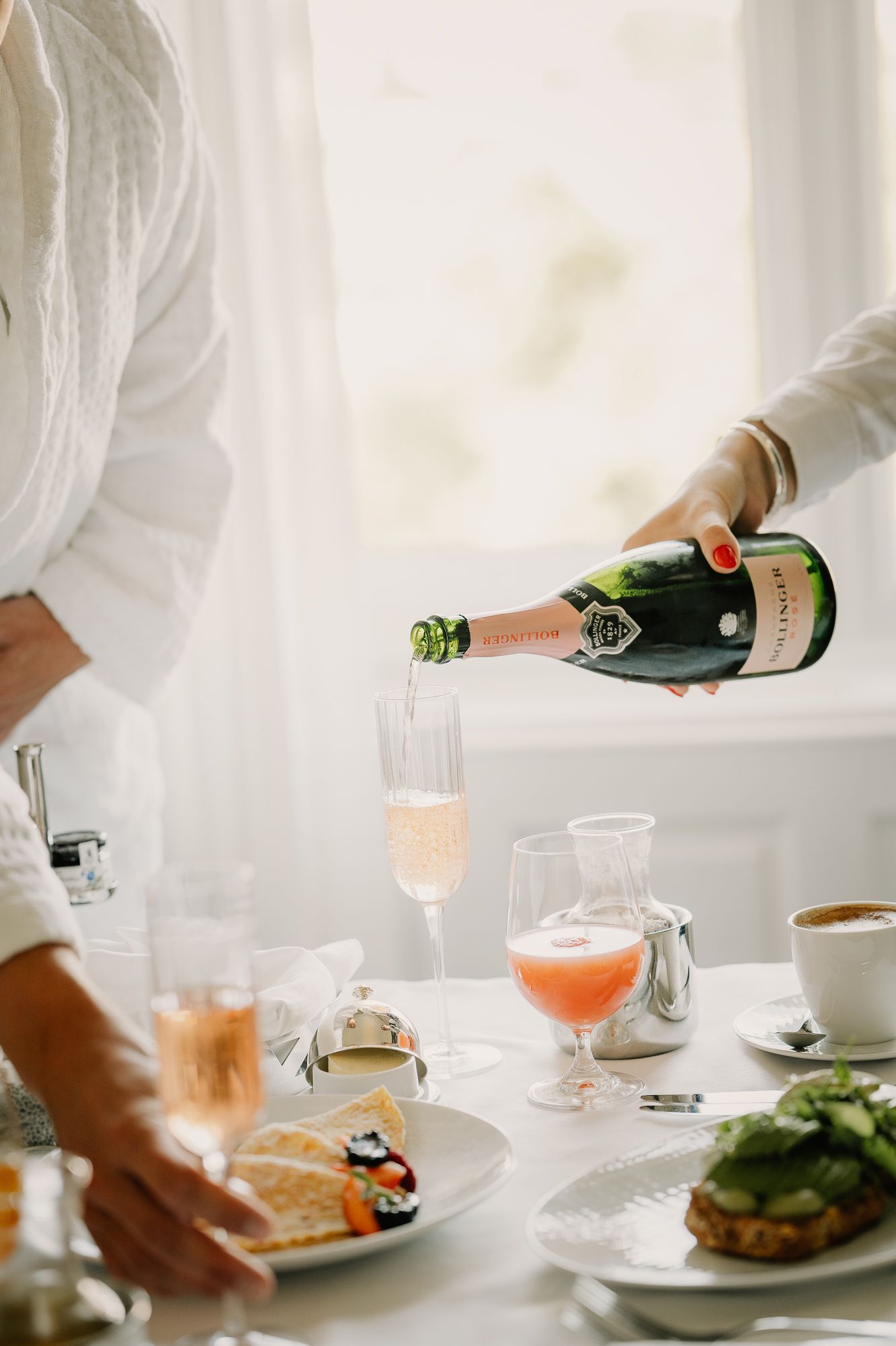 Person pouring rose champagne from a green bottle into a flute at an elegant brunch table setting.