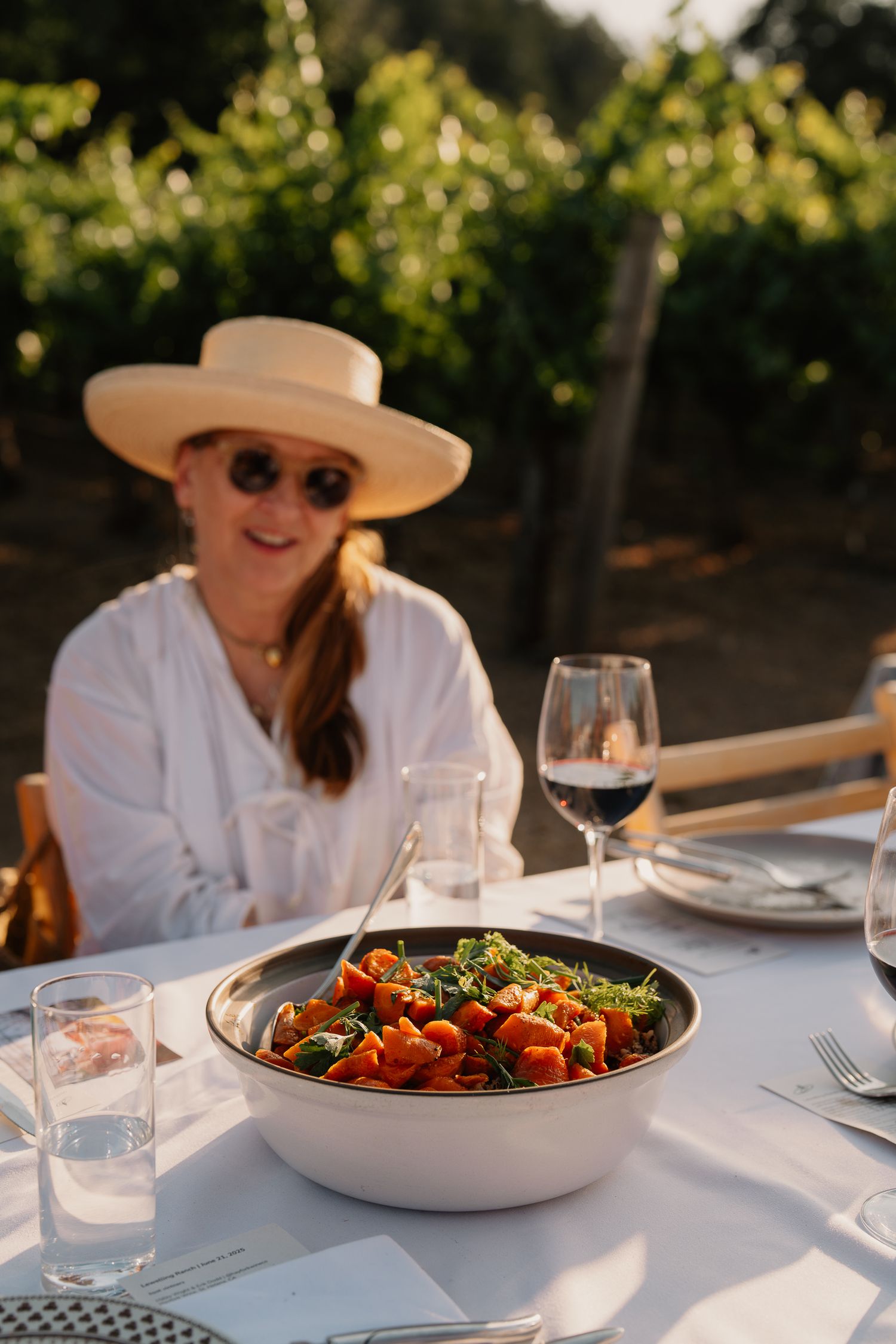 Fresh tomato salad served in white bowl at outdoor vineyard dining table with wine glass.